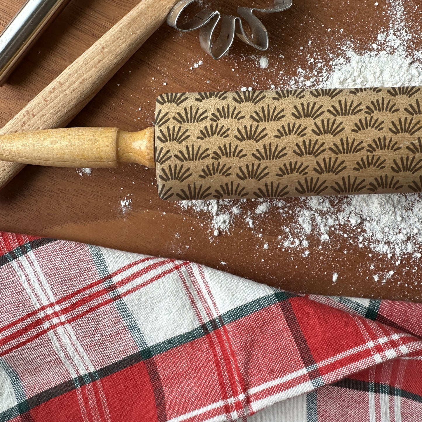 Rolling pin with decorative pattern on a wooden surface with flour and a plaid cloth.