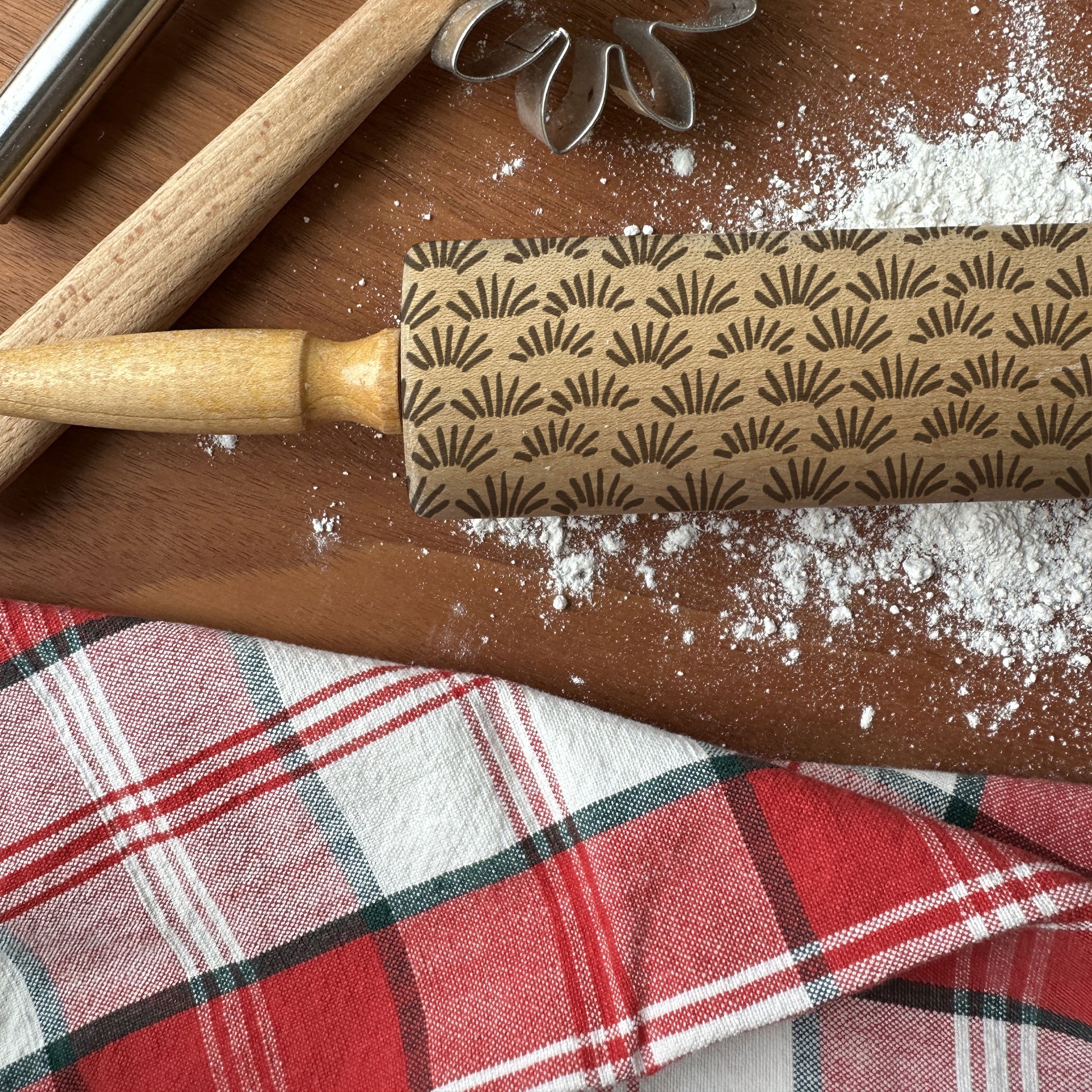 Rolling pin with decorative pattern on a wooden surface with flour and a plaid cloth.