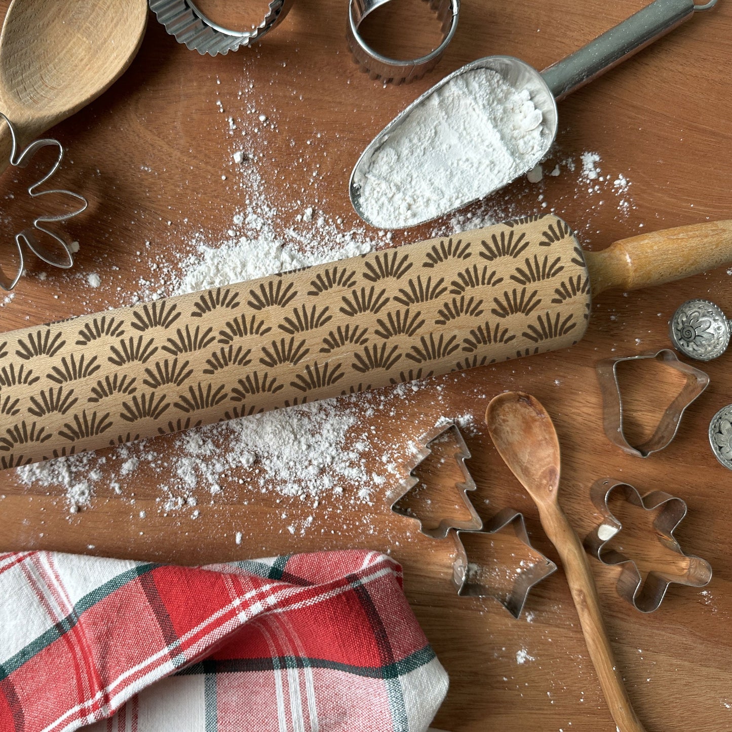 Baking tools including a patterned rolling pin, cookie cutters, and flour on a wooden surface.