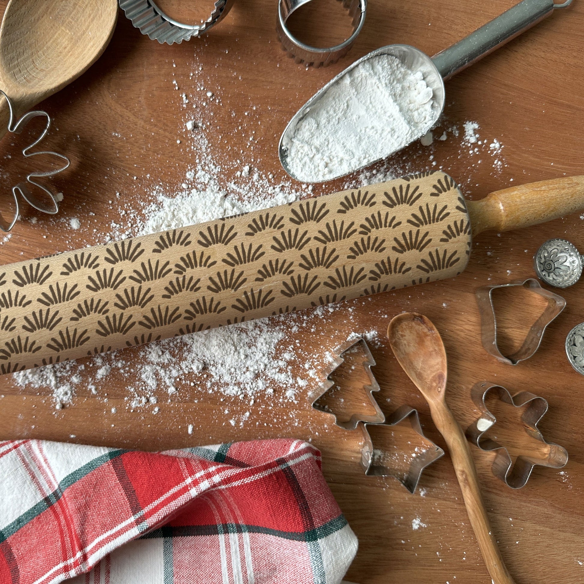Baking tools including a patterned rolling pin, cookie cutters, and flour on a wooden surface.