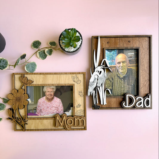 Two wooden picture frames with photos of a woman and a man, placed on a pink surface with decorative elements.