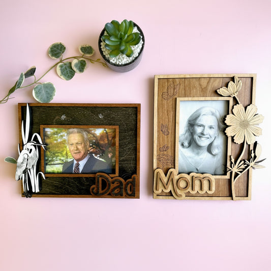 Two wooden photo frames with engraved names on a pink background.