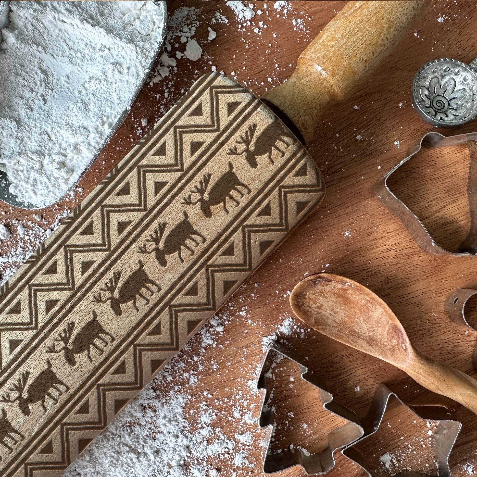 Wooden cookie cutters and a rolling pin with reindeer design on a wooden surface with flour.