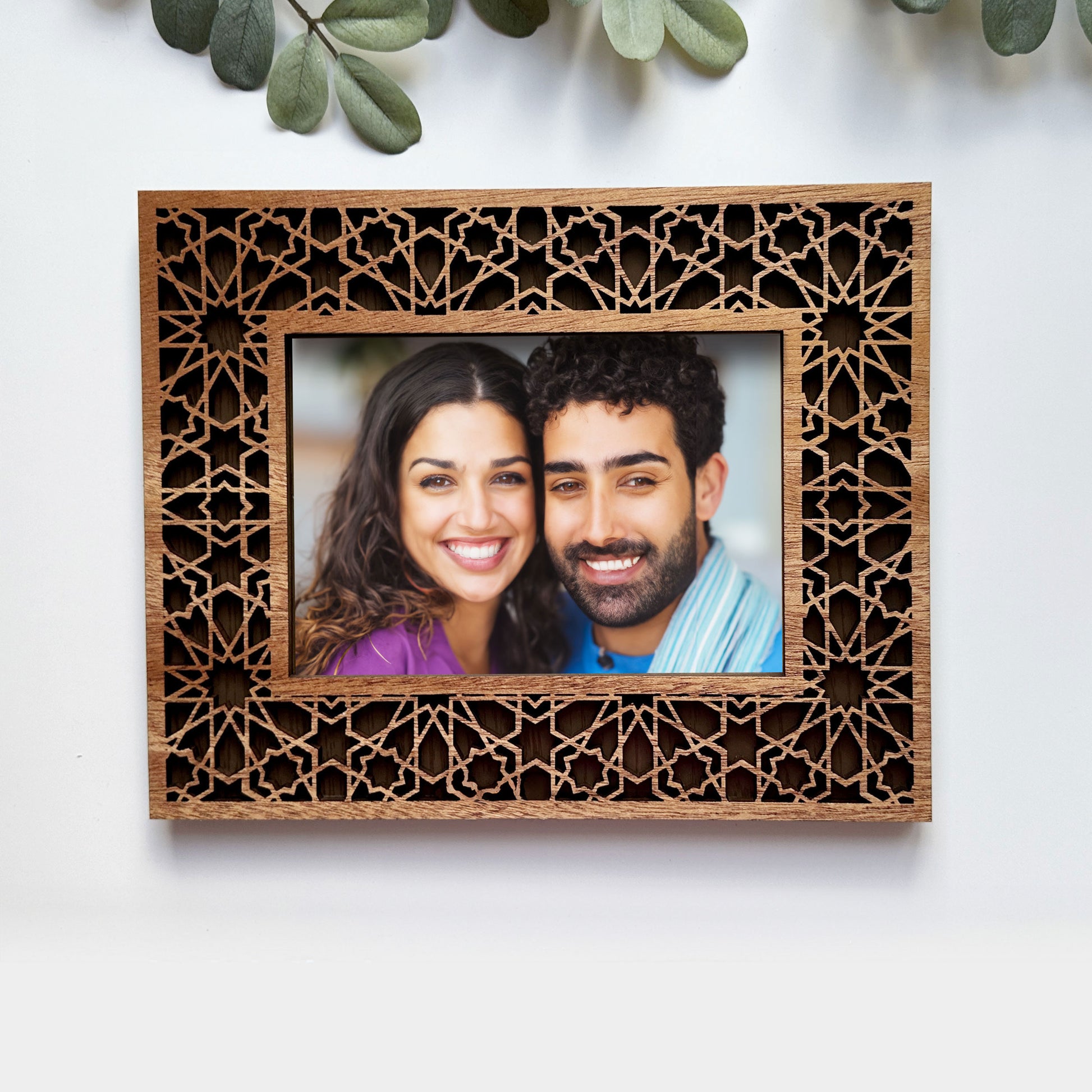 Wooden photo frame with intricate cut-out design, containing a photo of a couple, on a white background.