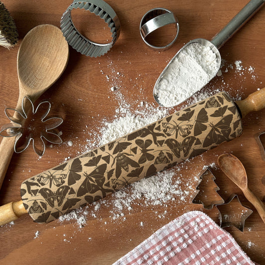 Baking tools including a rolling pin with embossed designs, wooden spoons, and cookie cutters on a wooden surface.