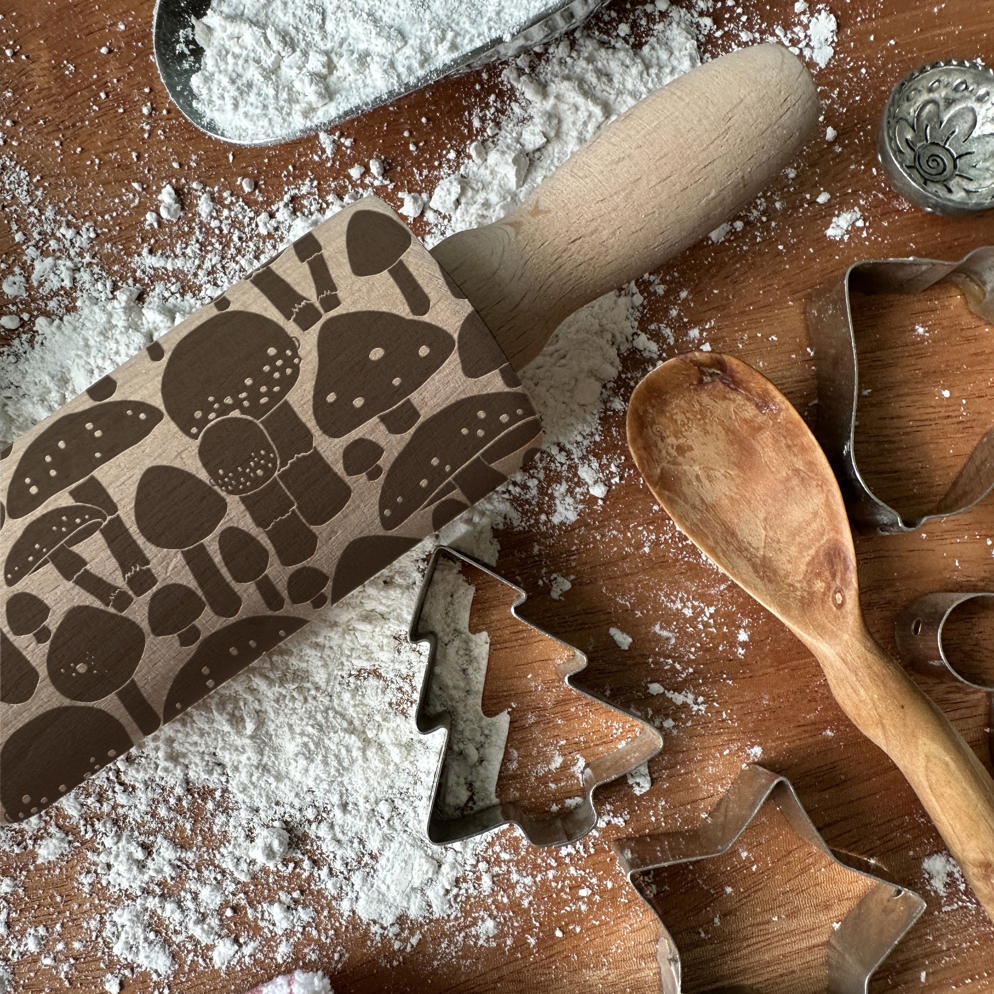 Rolling pin with mushroom pattern and cookie cutters on a flour-dusted surface