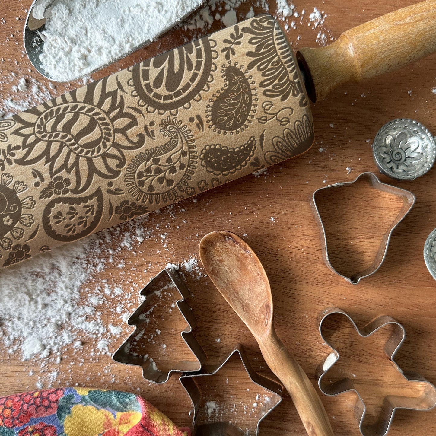 Baking tools including a patterned rolling pin and cookie cutters on a wooden surface with flour.