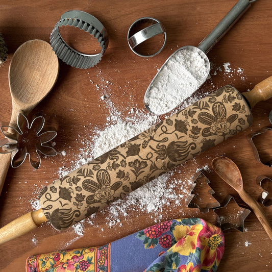 Decorative rolling pin with floral patterns on a wooden surface with flour and cookie cutters.