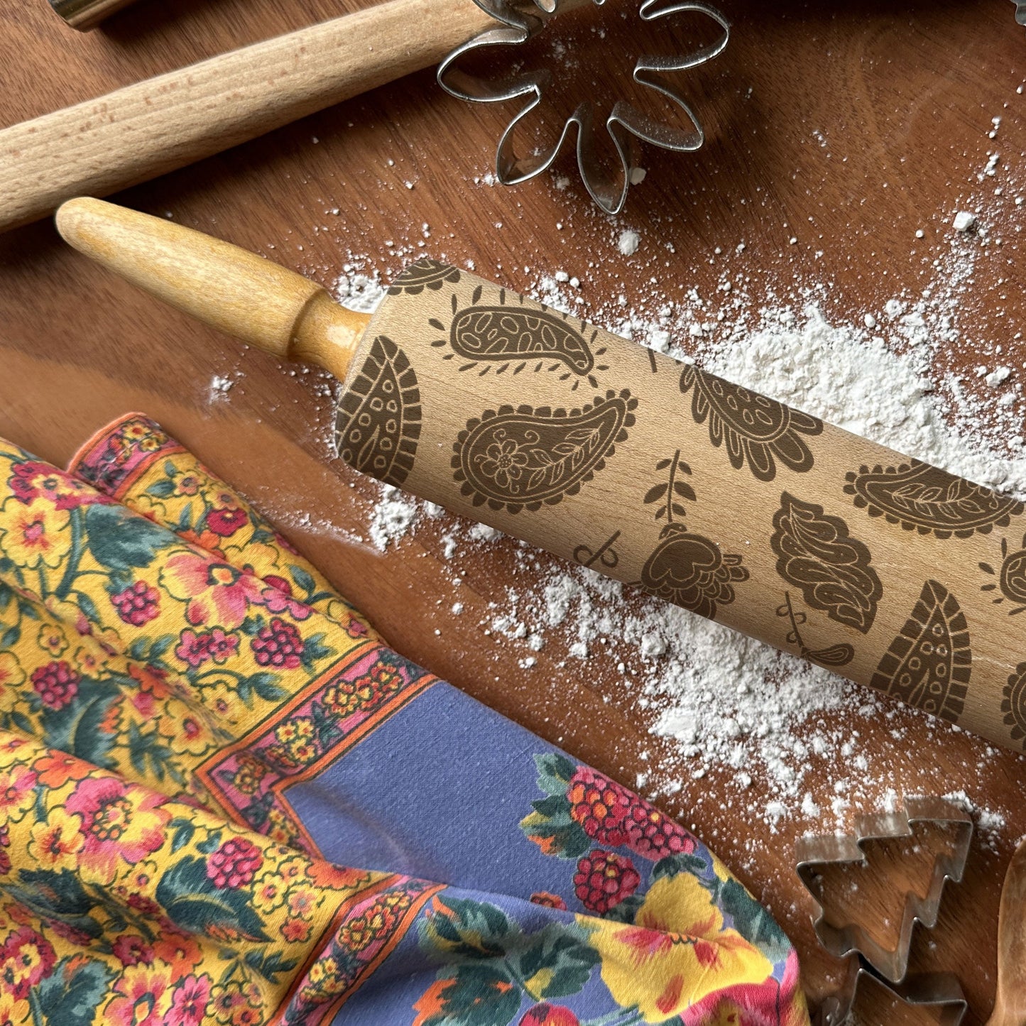 Decorative rolling pin with paisley patterns on a wooden surface with flour and baking tools.
