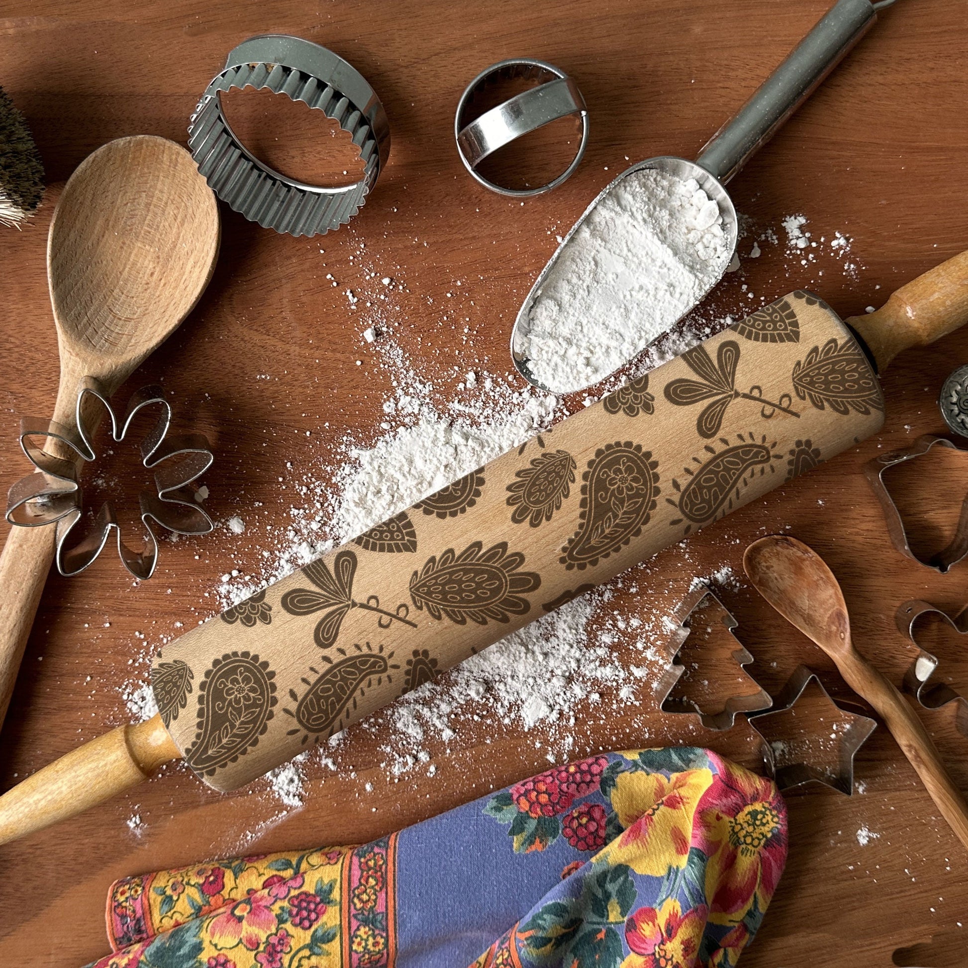Decorative rolling pin with floral patterns on a wooden surface with flour and baking tools.