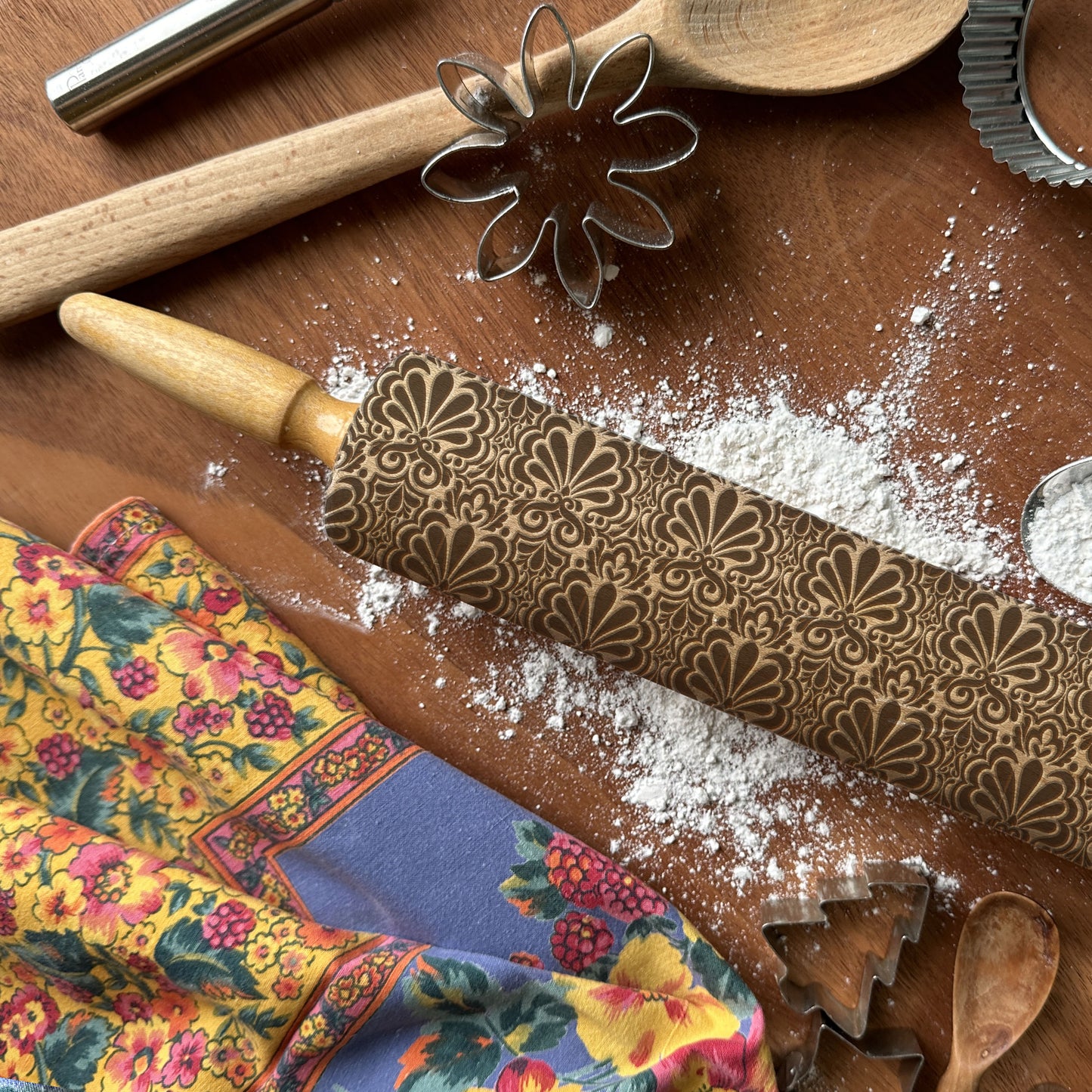 Decorative rolling pin with floral patterns on a wooden surface with flour and baking tools.