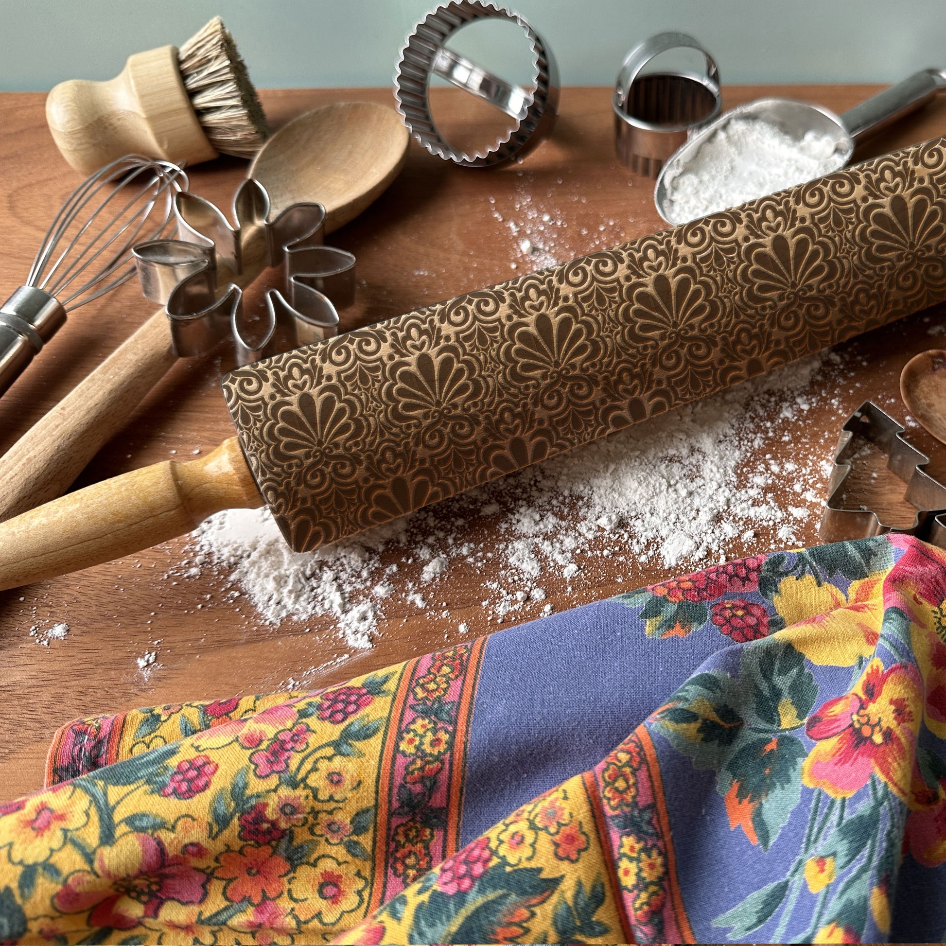 Decorative rolling pin with embossed pattern on a wooden surface with kitchen utensils and a colorful towel.