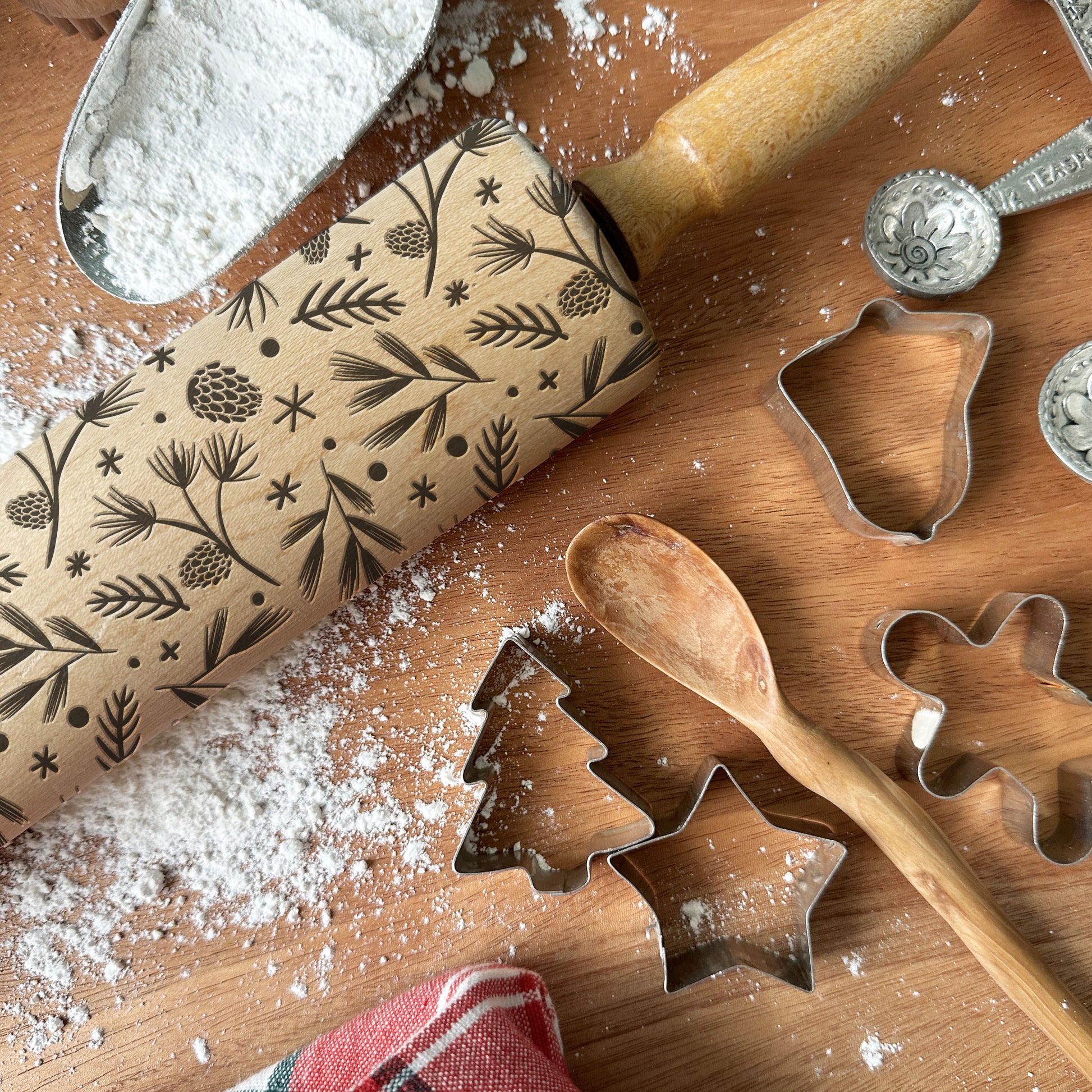 Baking tools including a rolling pin with embossed designs, cookie cutters, and flour on a wooden surface.