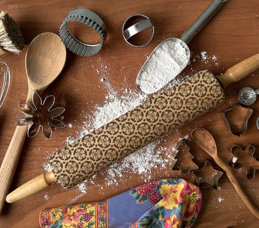 Decorative rolling pin with floral pattern on a wooden surface with kitchen utensils and flour.