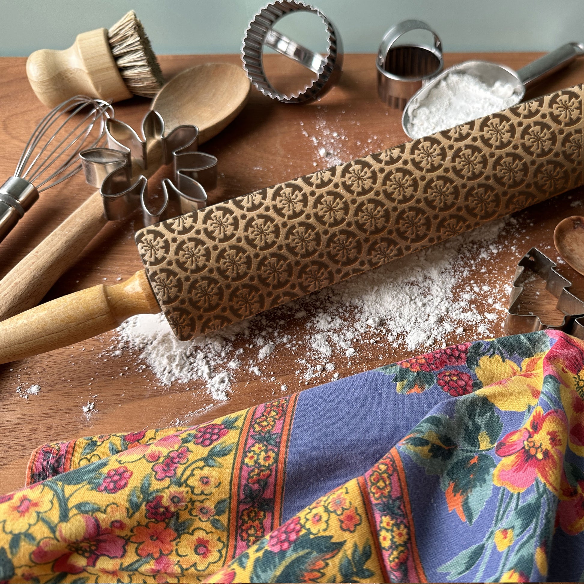 Decorative rolling pin with floral patterns on a wooden surface with baking tools and flour.