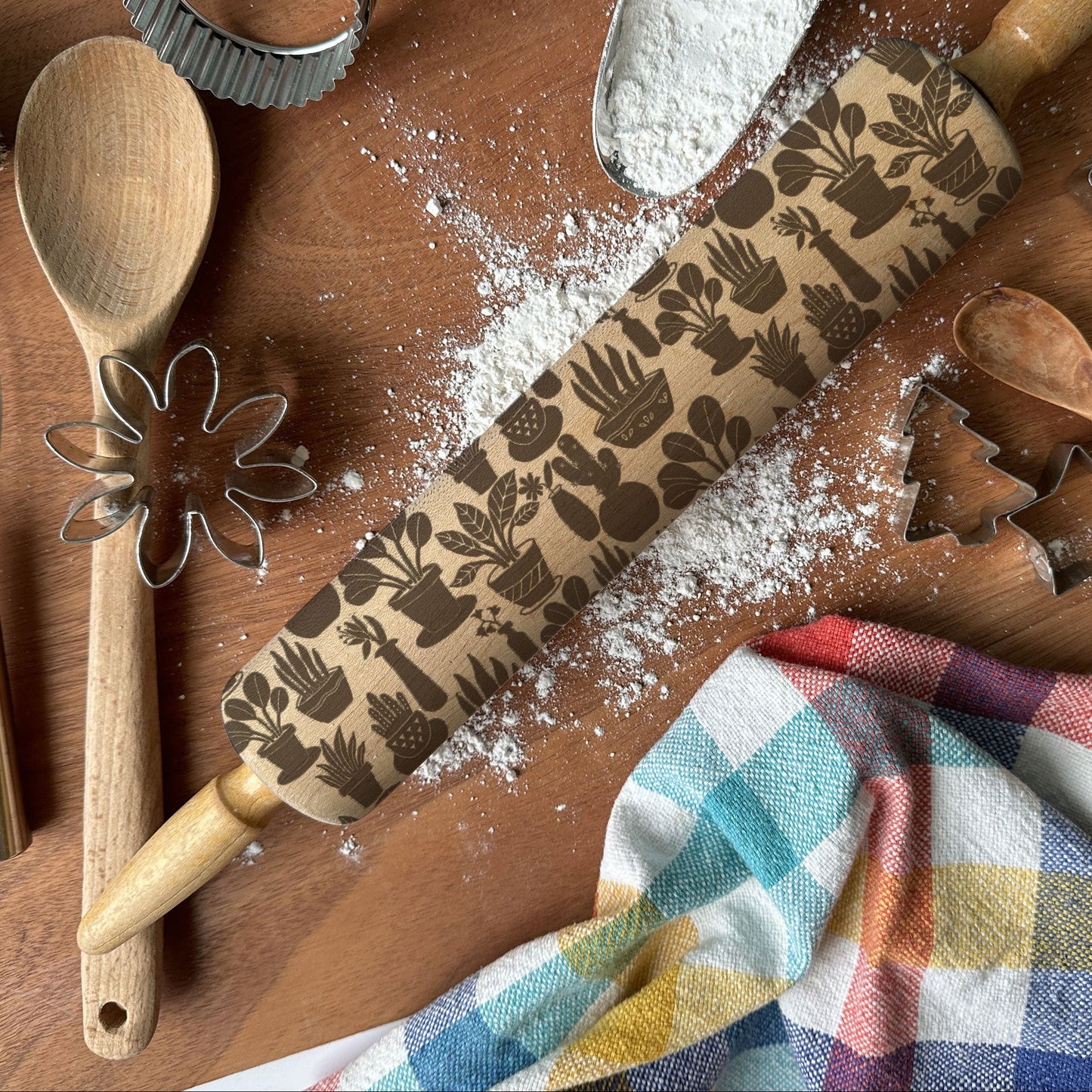 Baking tools including a rolling pin with embossed designs, wooden spoon, whisk, and cookie cutters on a wooden surface.