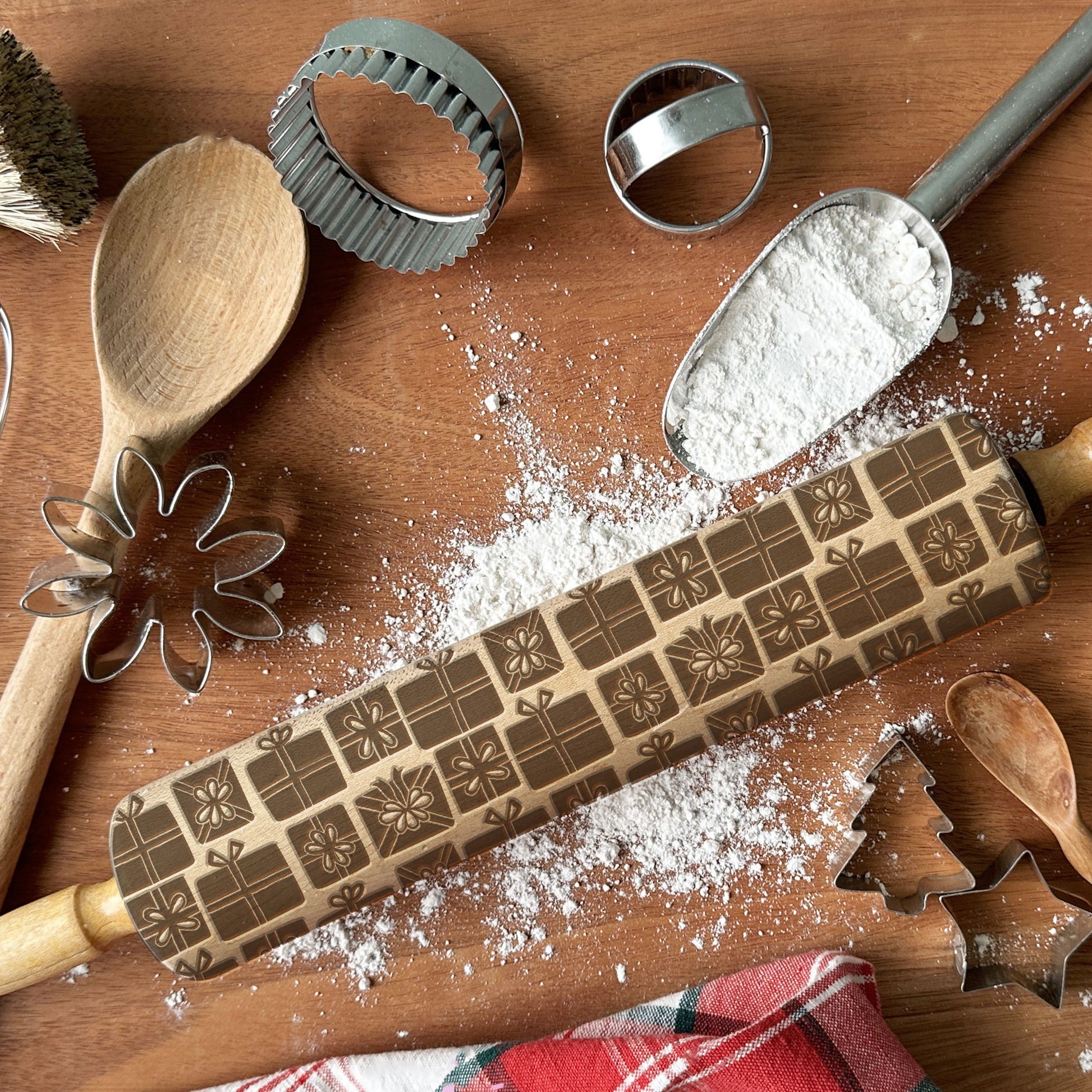 Wooden rolling pin with embossed designs on a wooden surface with flour and kitchen utensils.