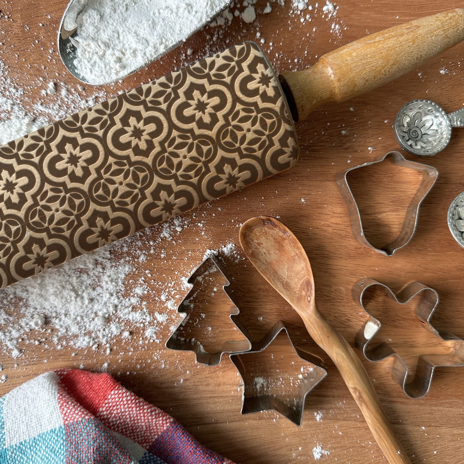Wooden rolling pin with leaf pattern and cookie cutters on a wooden surface with flour.