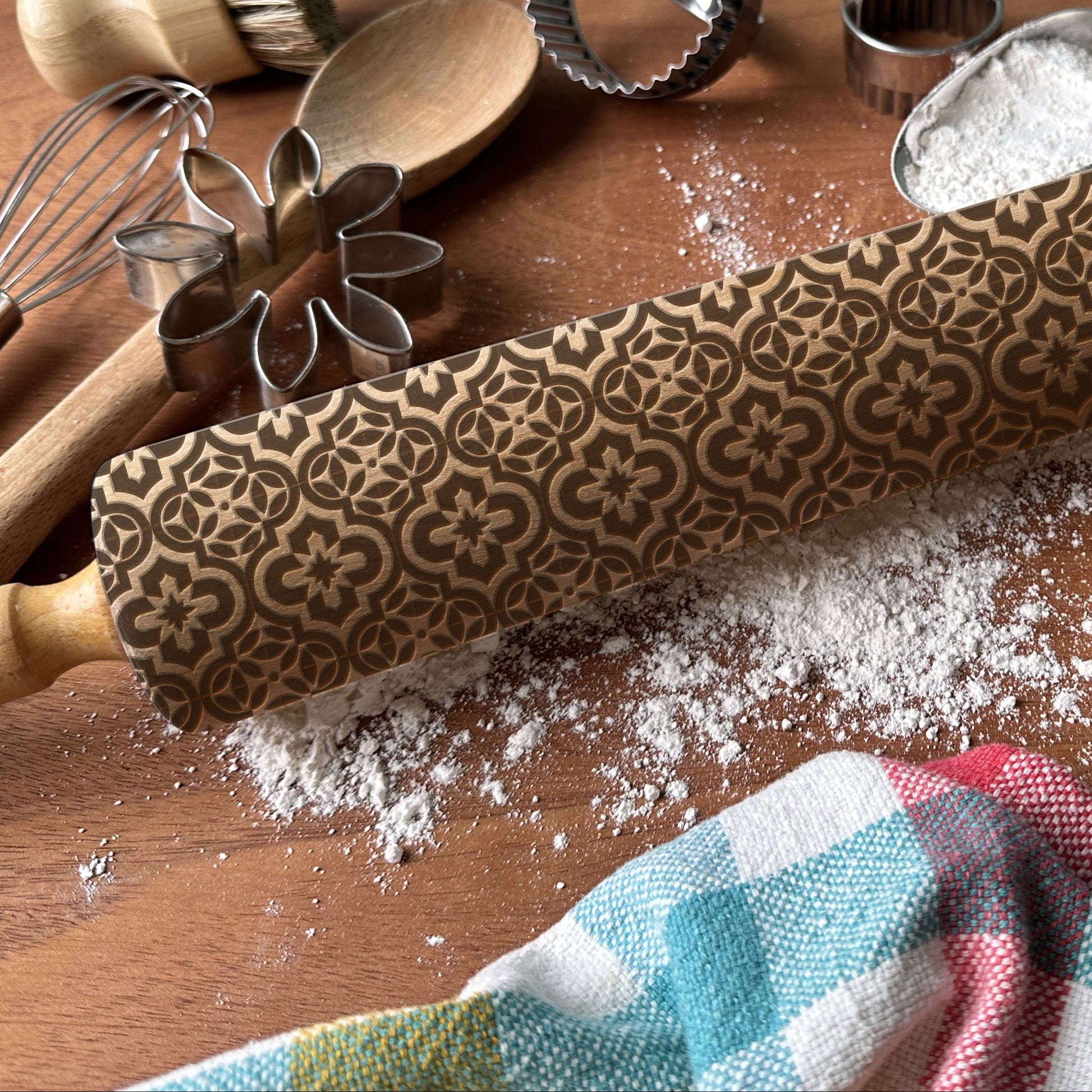 Decorative rolling pin with floral patterns on a wooden surface with flour and kitchen tools.