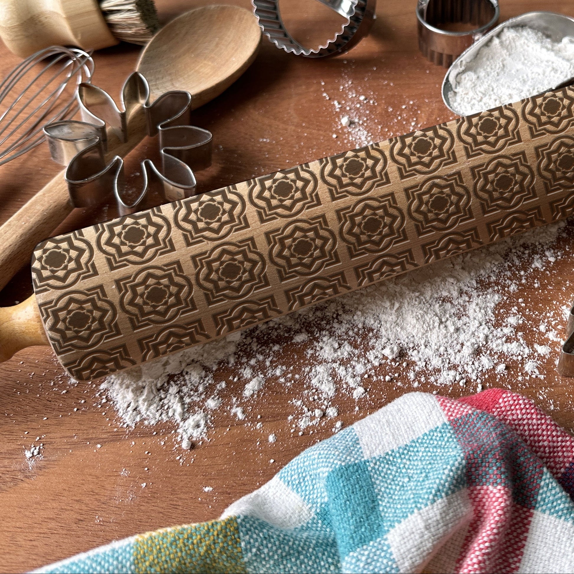 Decorative rolling pin with embossed patterns on a wooden surface with baking tools.