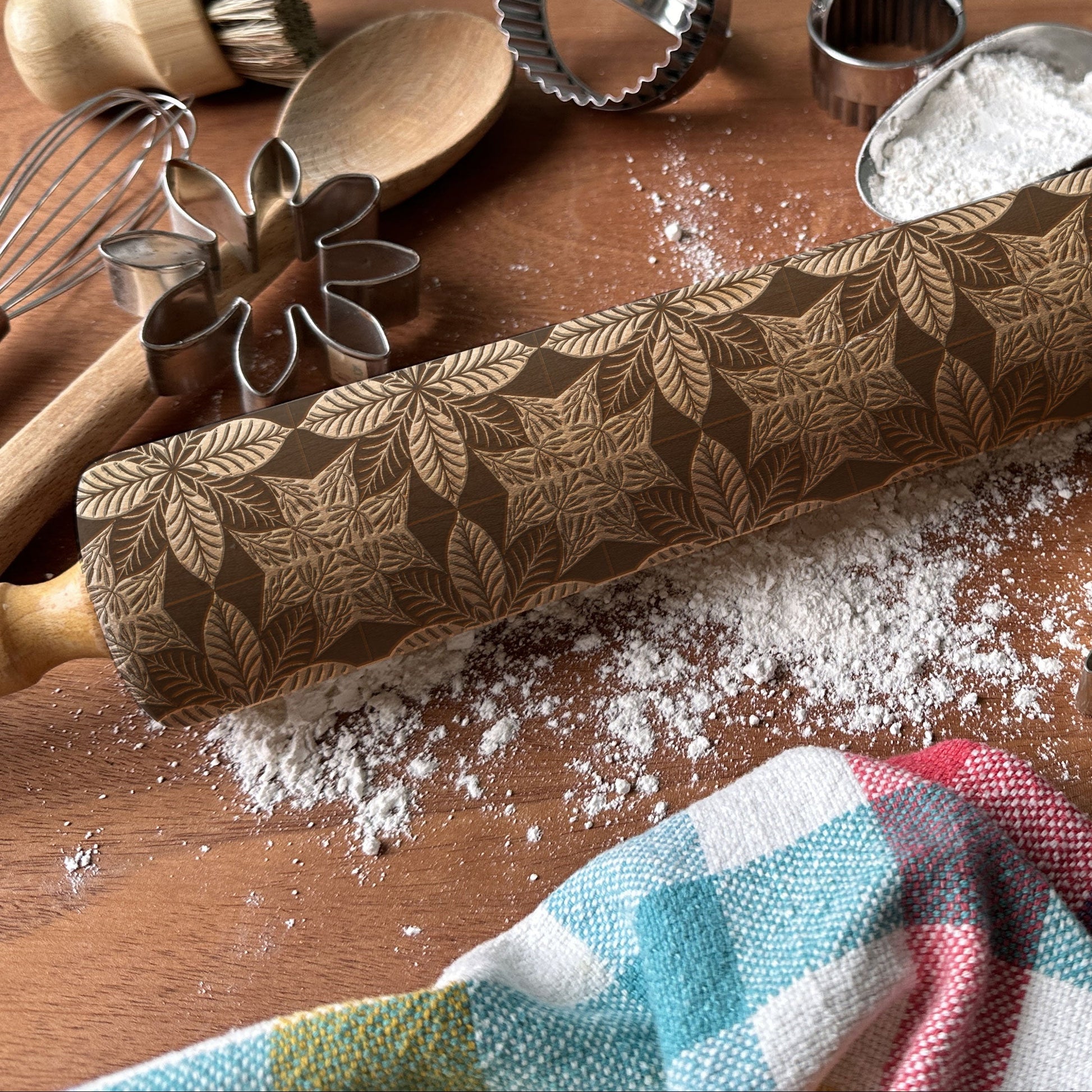 Decorative rolling pin with leaf pattern on a wooden surface with baking tools.