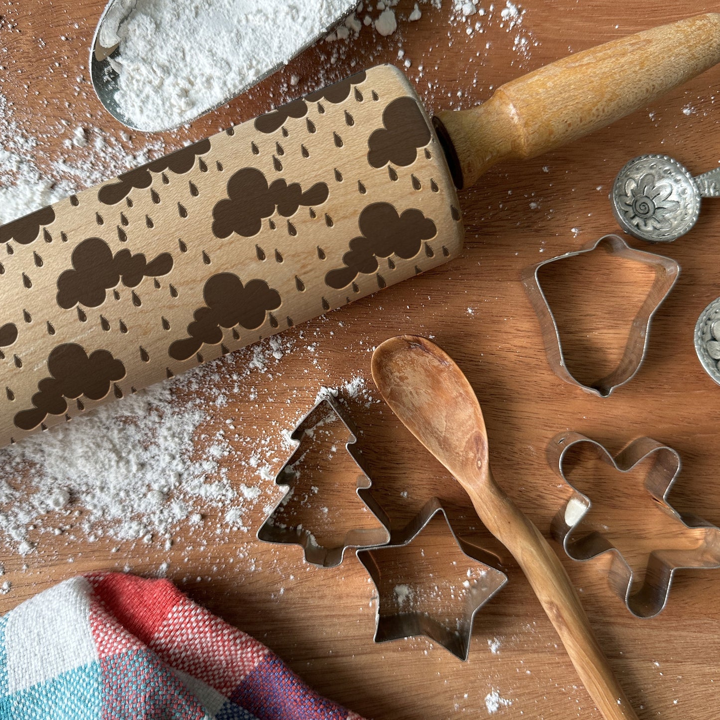 Wooden rolling pin with cloud pattern and cookie cutters on a wooden surface with flour.