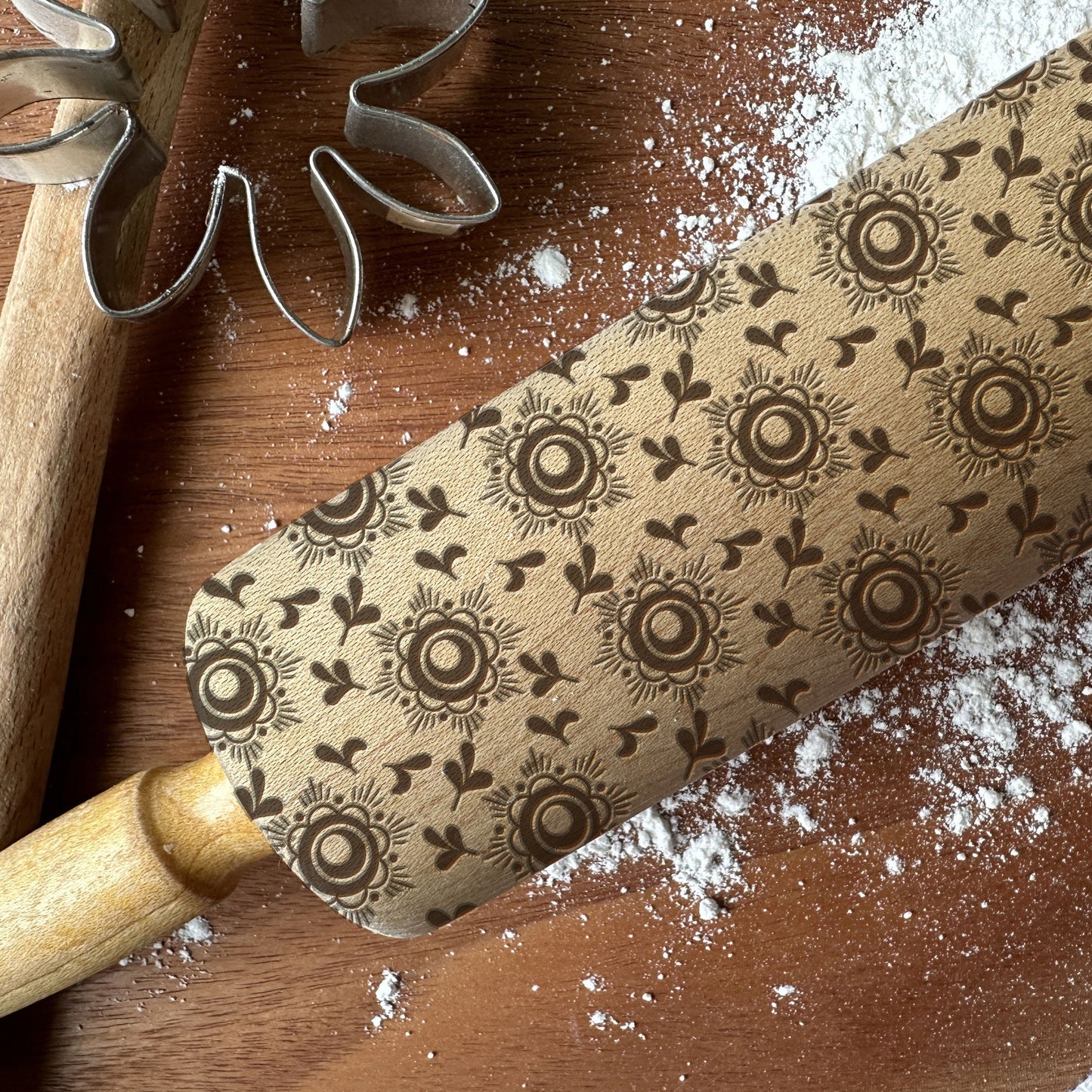 Decorative rolling pin with floral pattern on a wooden surface with flour.