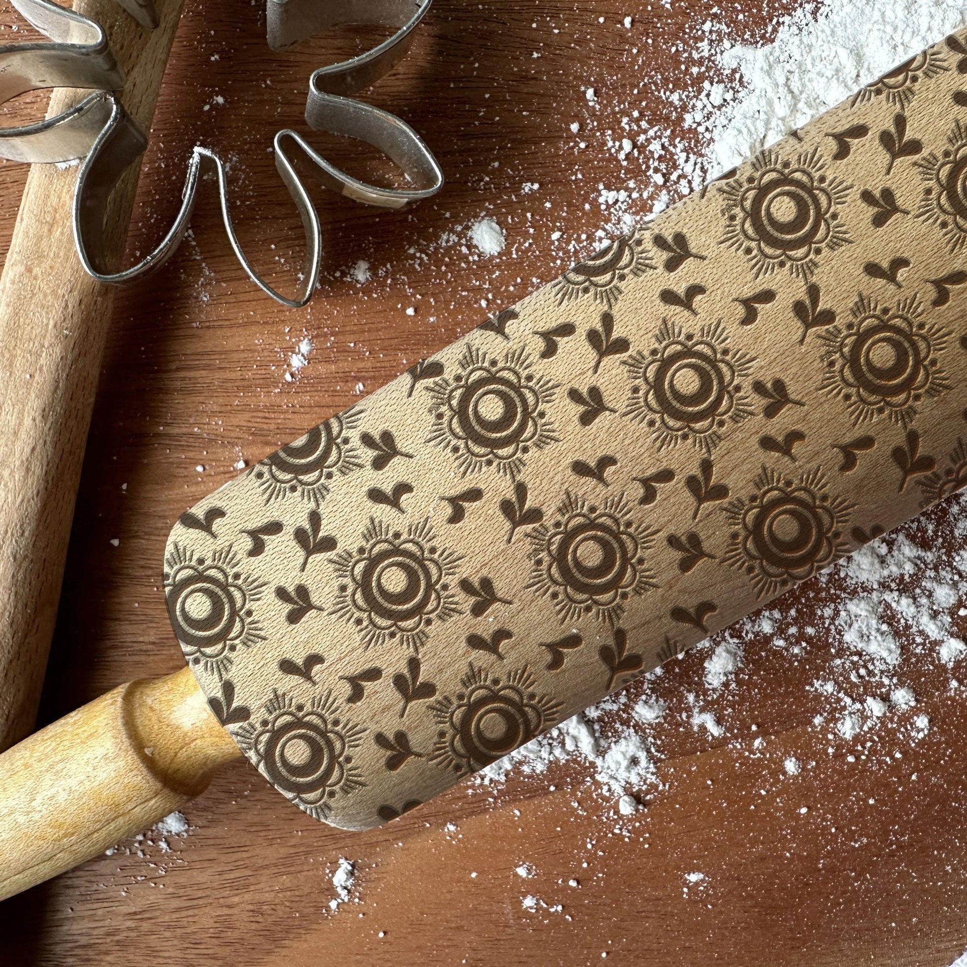 Decorative rolling pin with floral pattern on a wooden surface with flour.