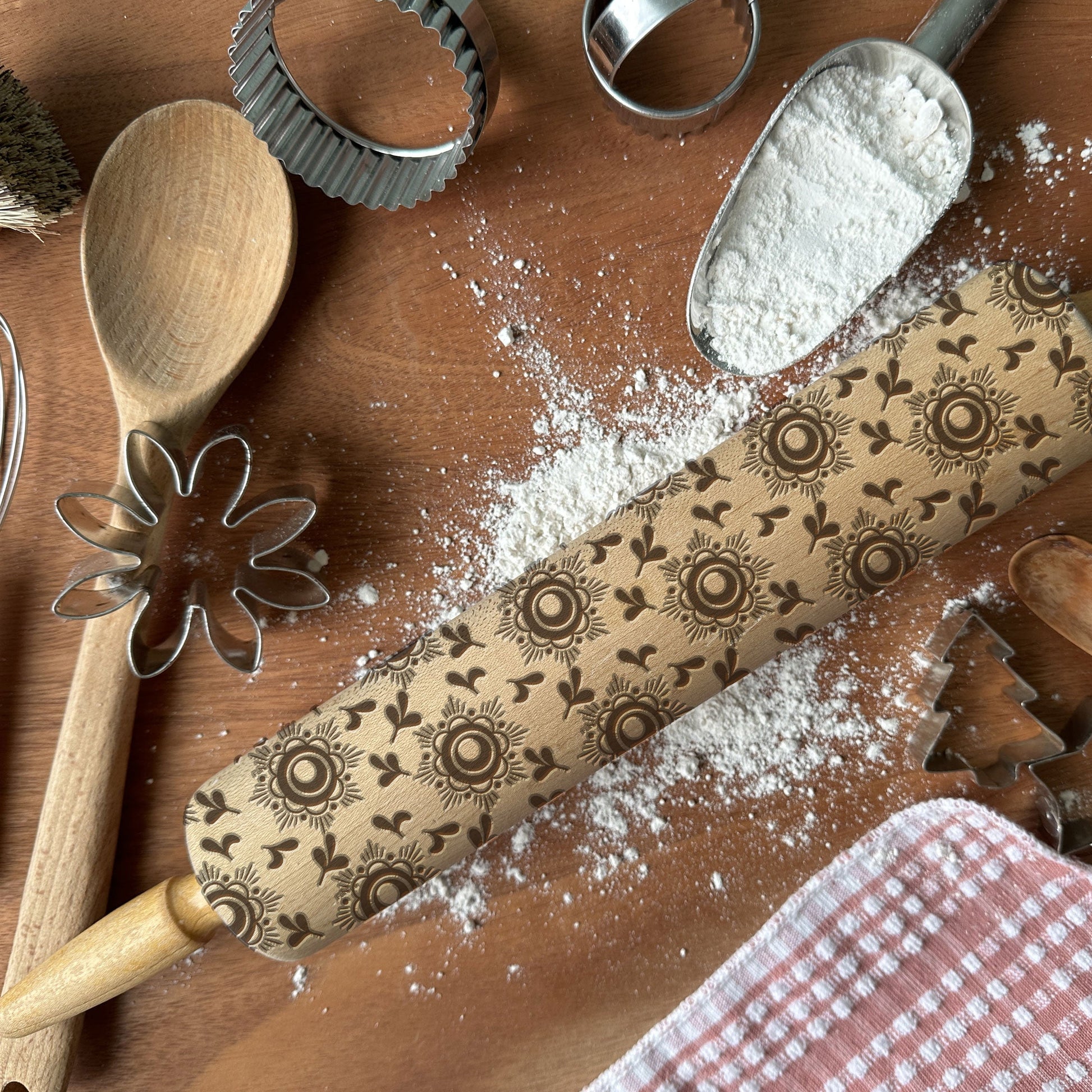 Decorative rolling pin with floral patterns on a wooden surface with flour and baking tools.