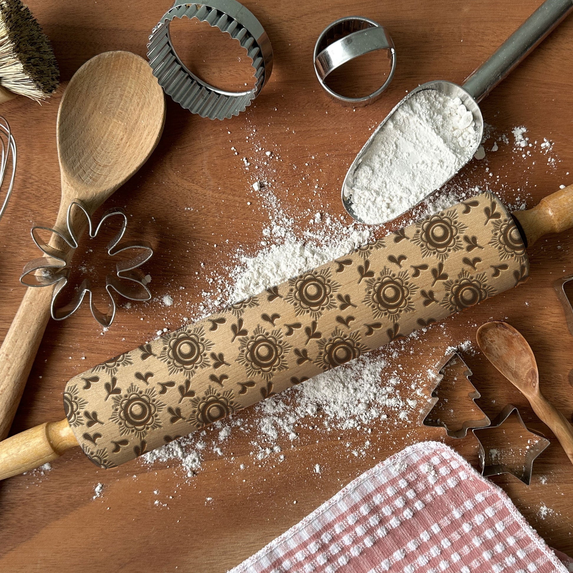 Decorative rolling pin with embossed patterns on a wooden surface with baking tools and flour.