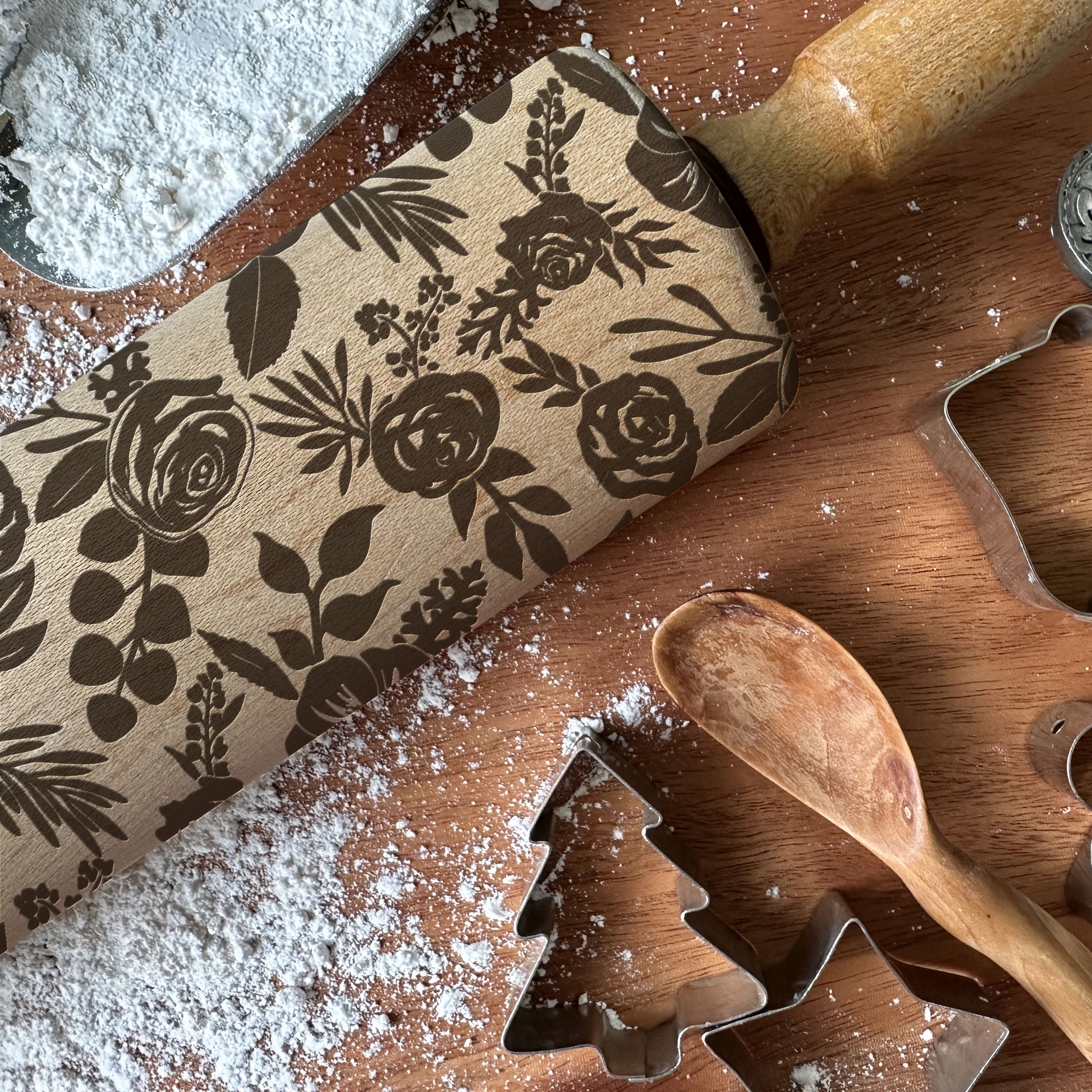 Floral-patterned rolling pin on a wooden surface with cookie cutters and flour.