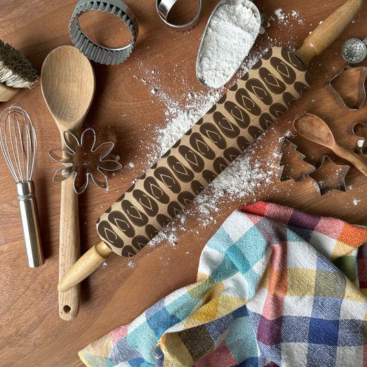 Wooden kitchen utensils including a rolling pin, spatula, and cookie cutters on a wooden surface with flour.
