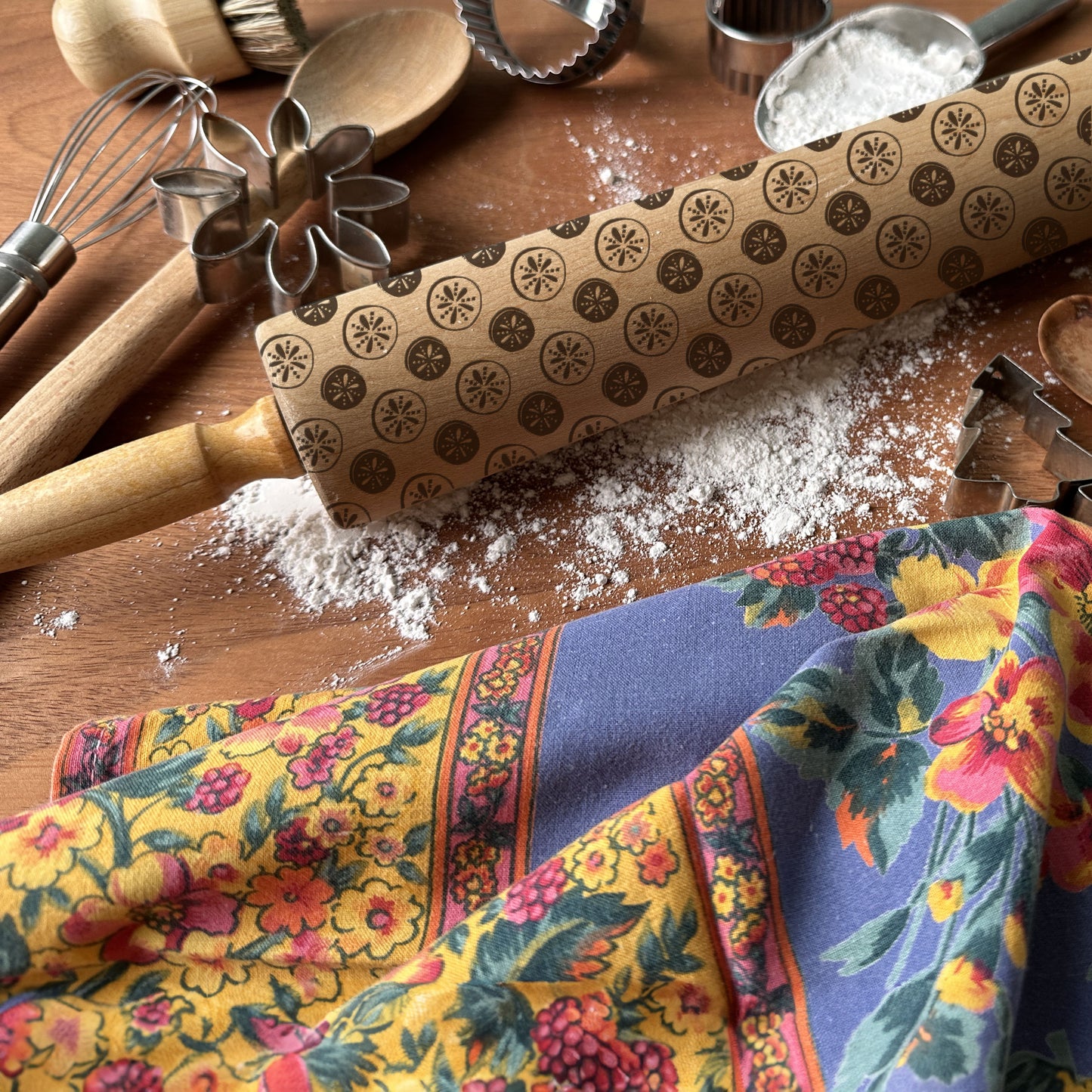 Rolling pin with pattern, flour, and colorful kitchen towel on a wooden surface