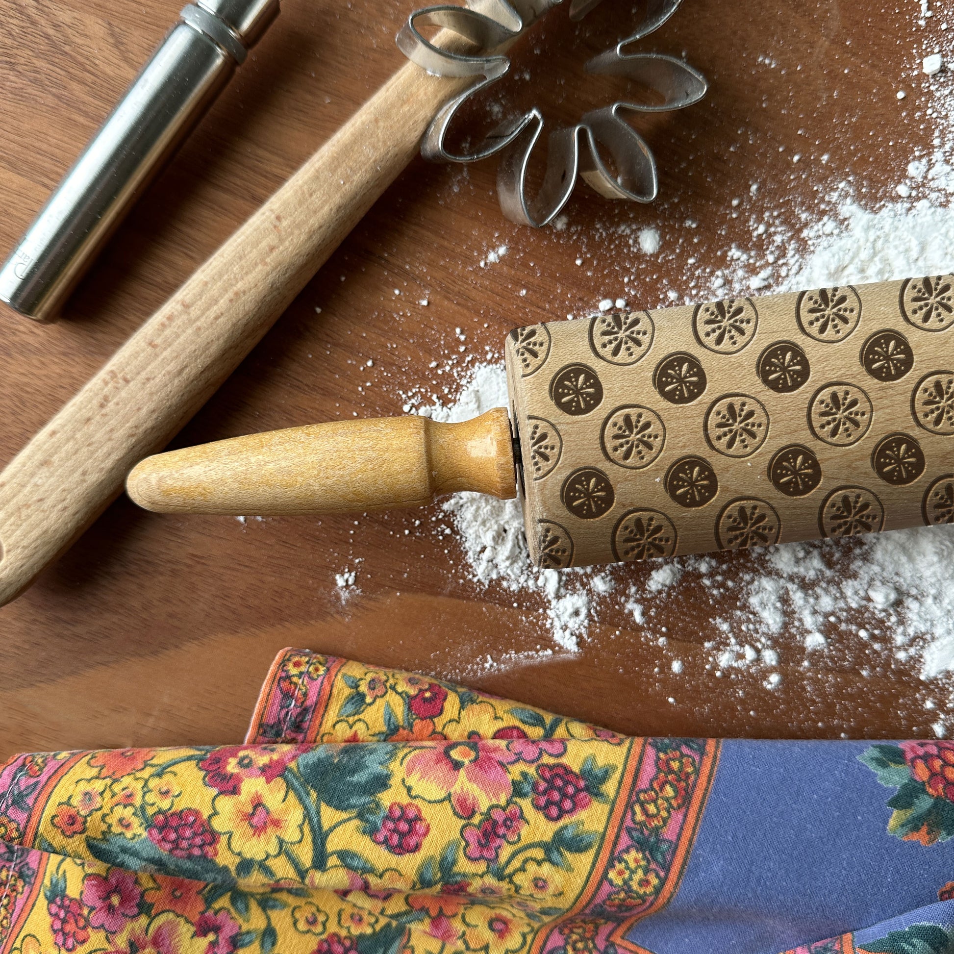 Decorative rolling pin with star patterns on a wooden surface with flour and a floral towel.