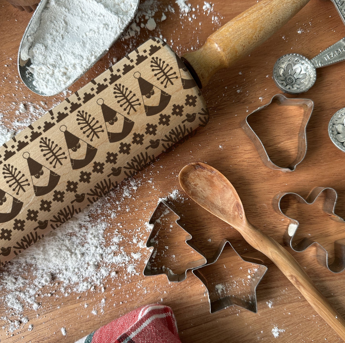 Baking tools including a rolling pin with embossing pattern, cookie cutters, and flour on a wooden surface.