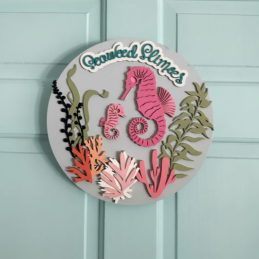 Decorative sign with seahorses, seaweed, and coral on a white background