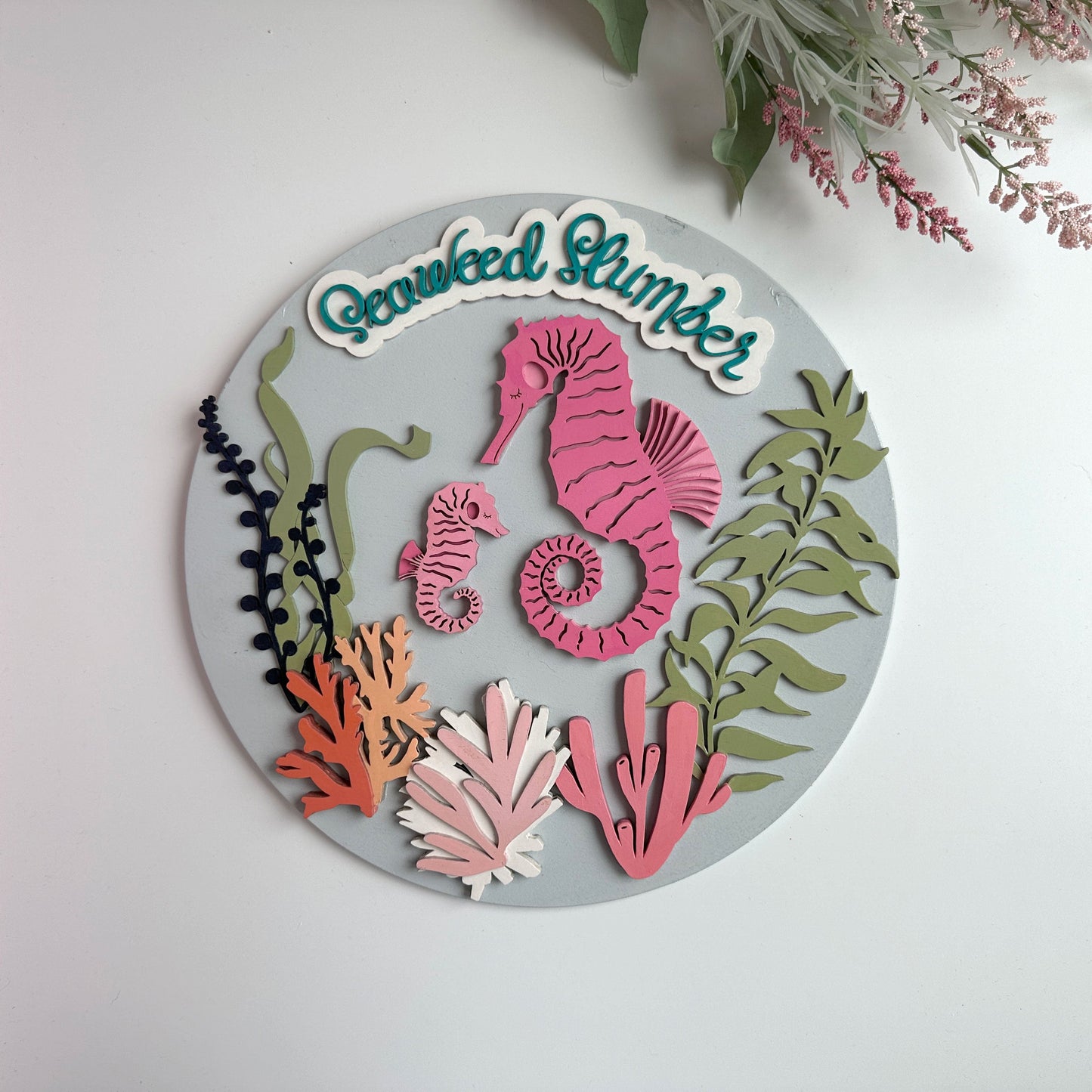 Decorative wall art with pink seahorses and seaweed on a gray background