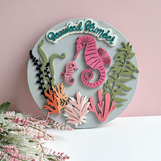 Decorative wall art with seahorse and seaweed design on a pink background