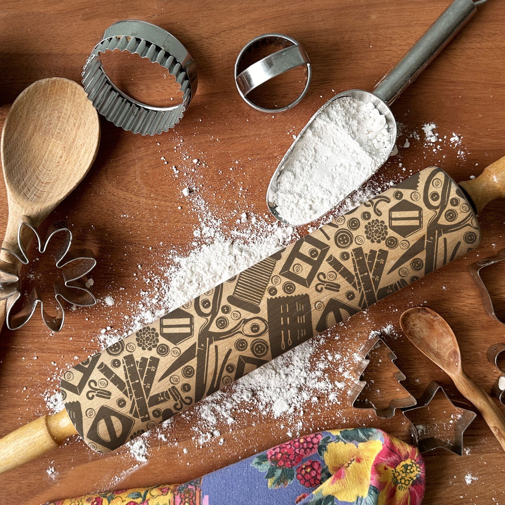 Baking tools including a wooden rolling pin with decorative patterns, wooden spoons, and cookie cutters on a wooden surface.