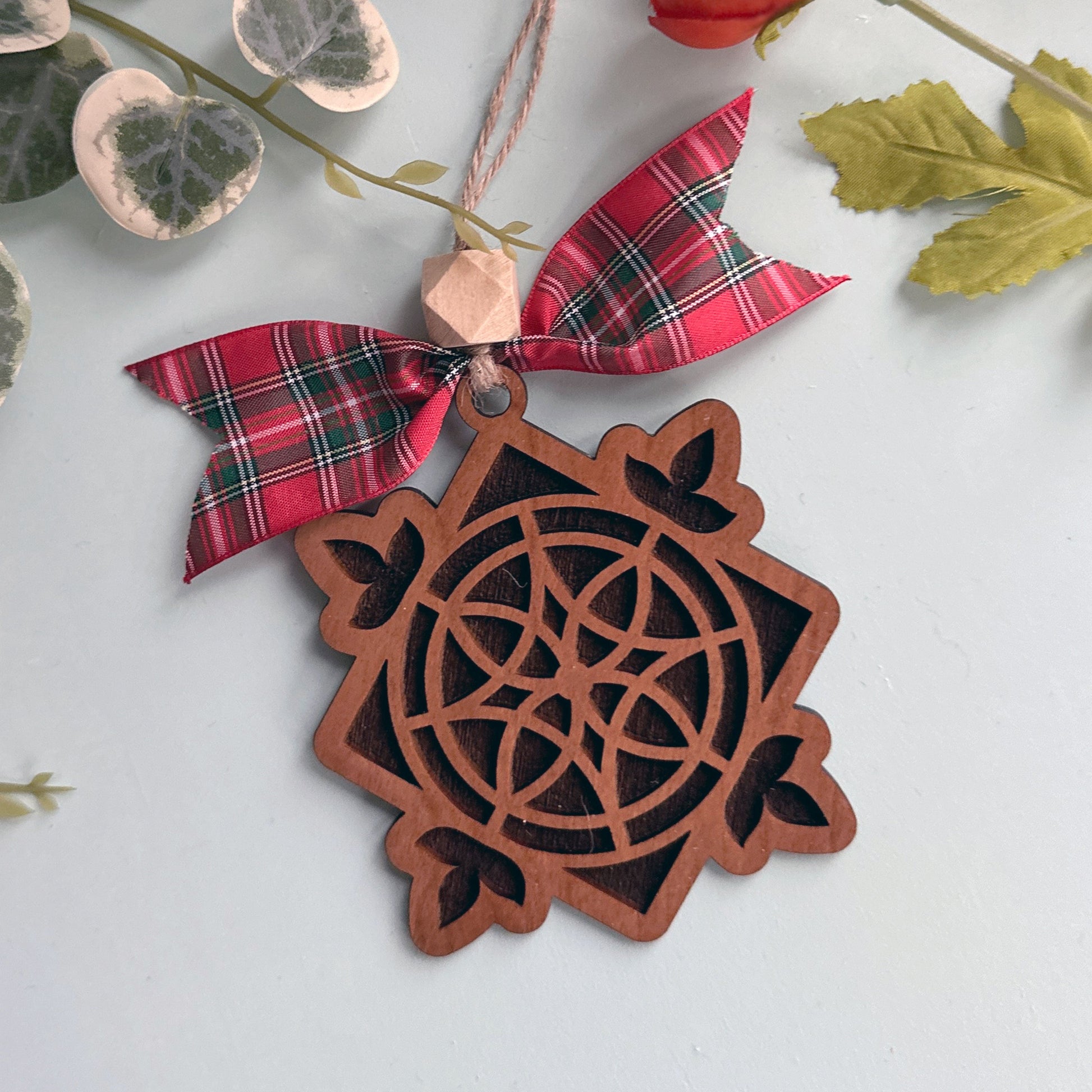 Decorative wooden ornament with a red plaid bow on a light background