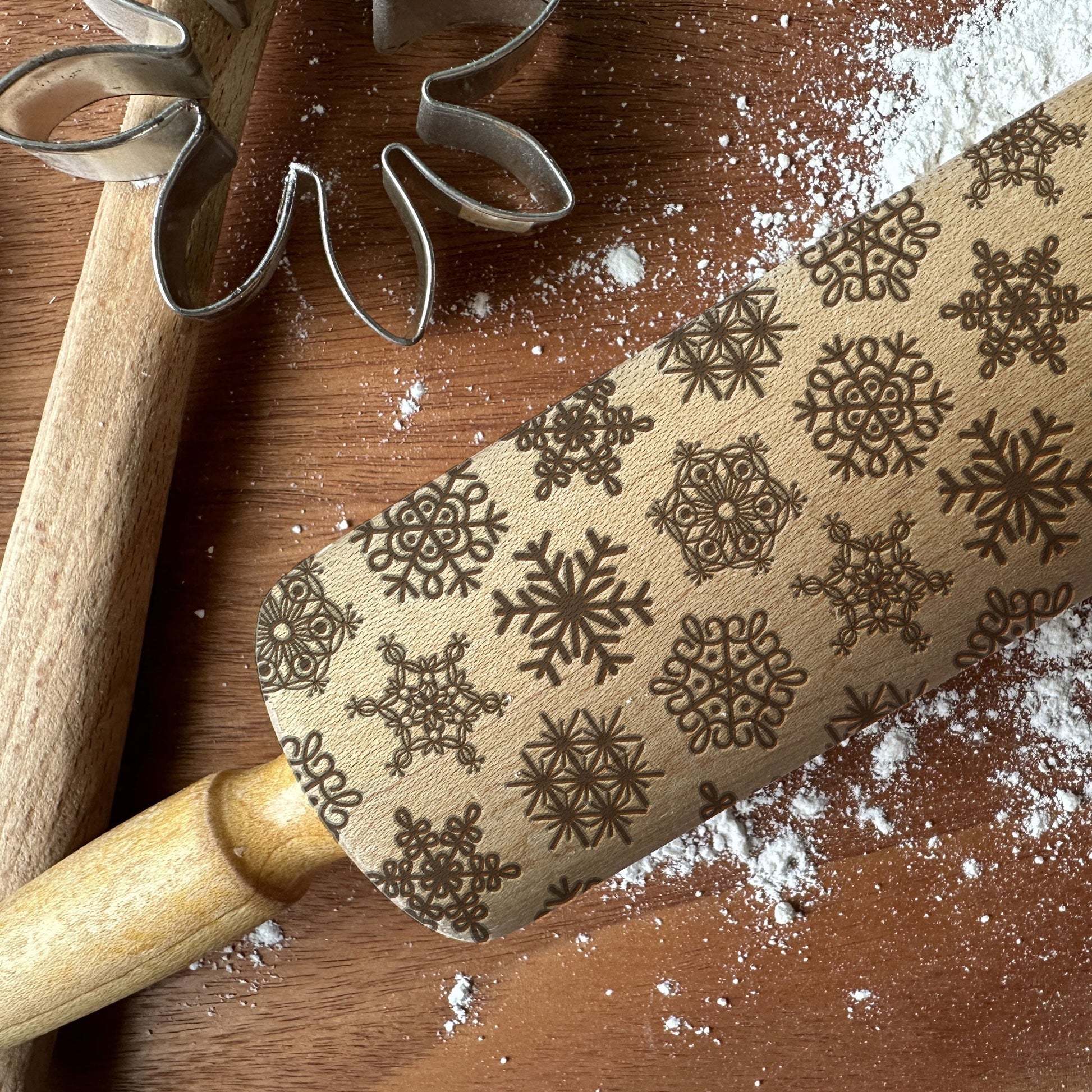 Wooden rolling pin with snowflake patterns on a wooden surface with flour.