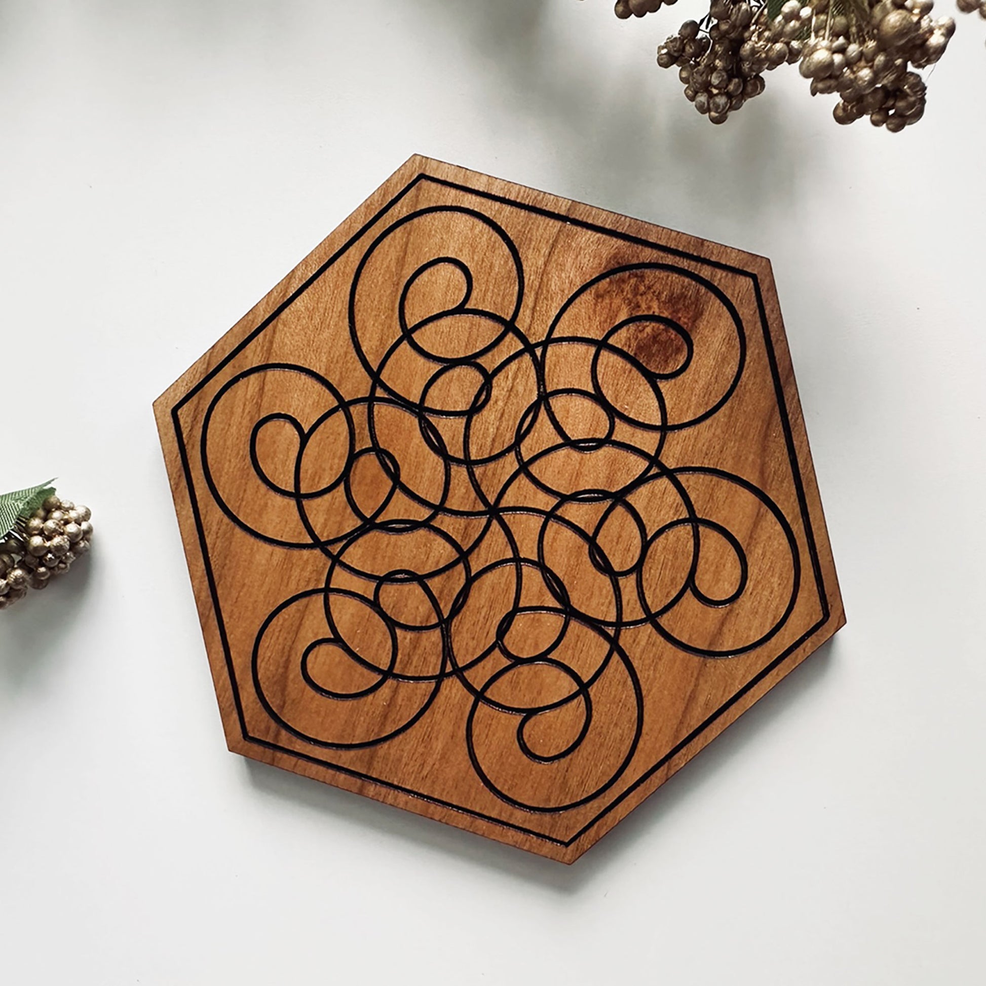 Hexagonal wooden coaster with intricate black laser-cut design on a light background