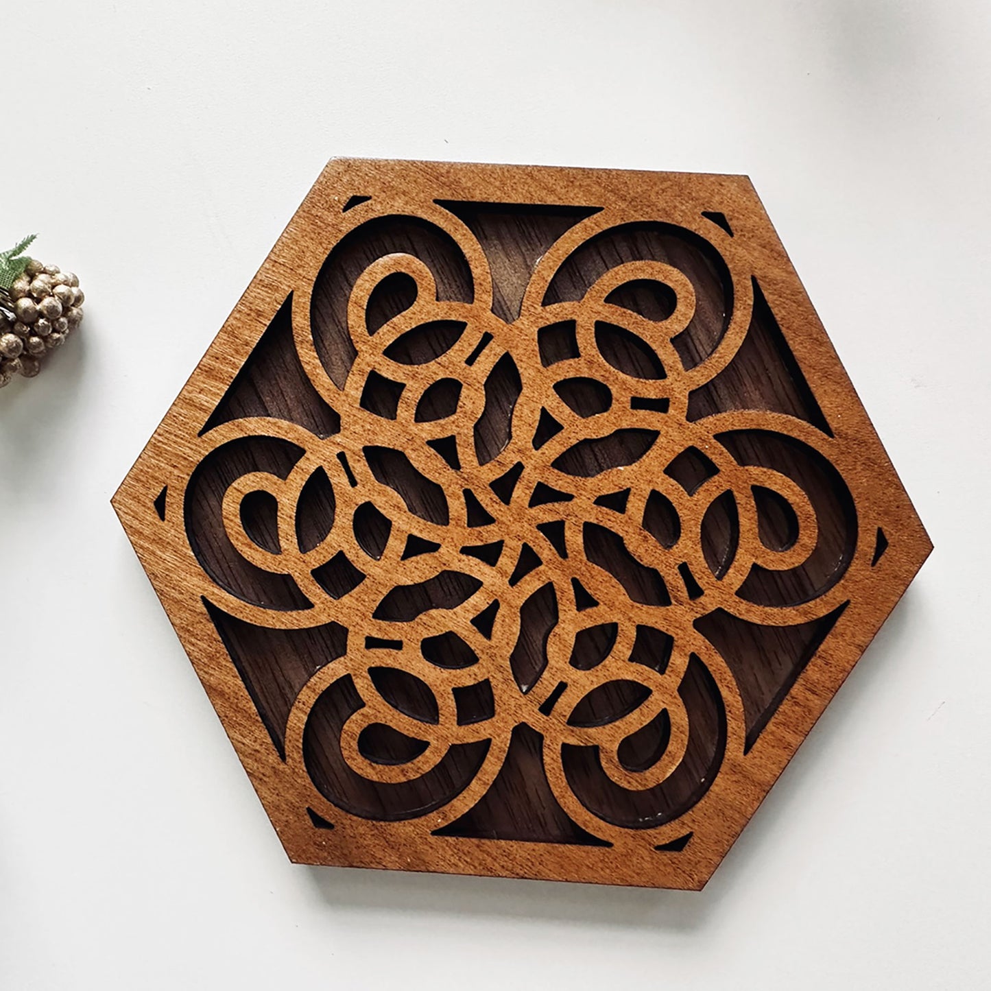 Hexagonal wooden coaster with intricate cut-out design on a white background