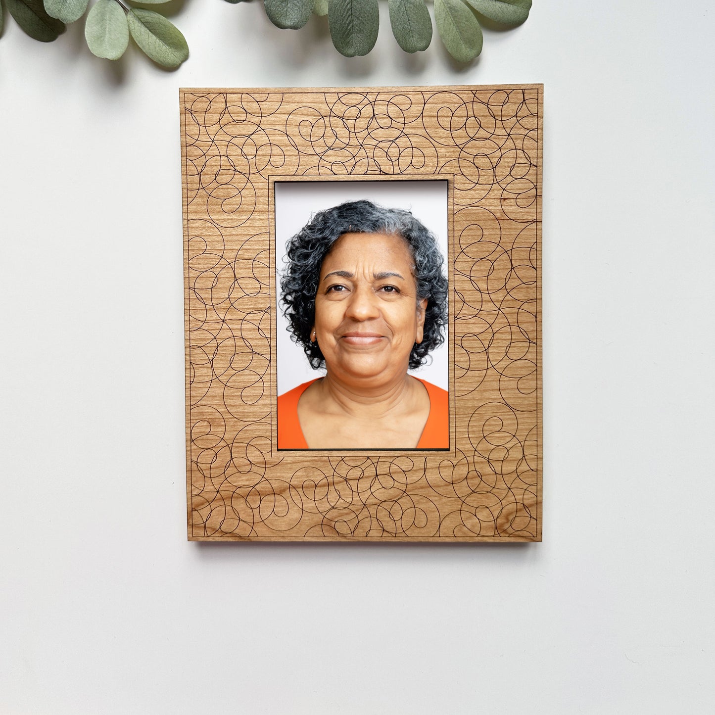 Wooden photo frame with a decorative pattern containing a portrait of a woman on a white wall.