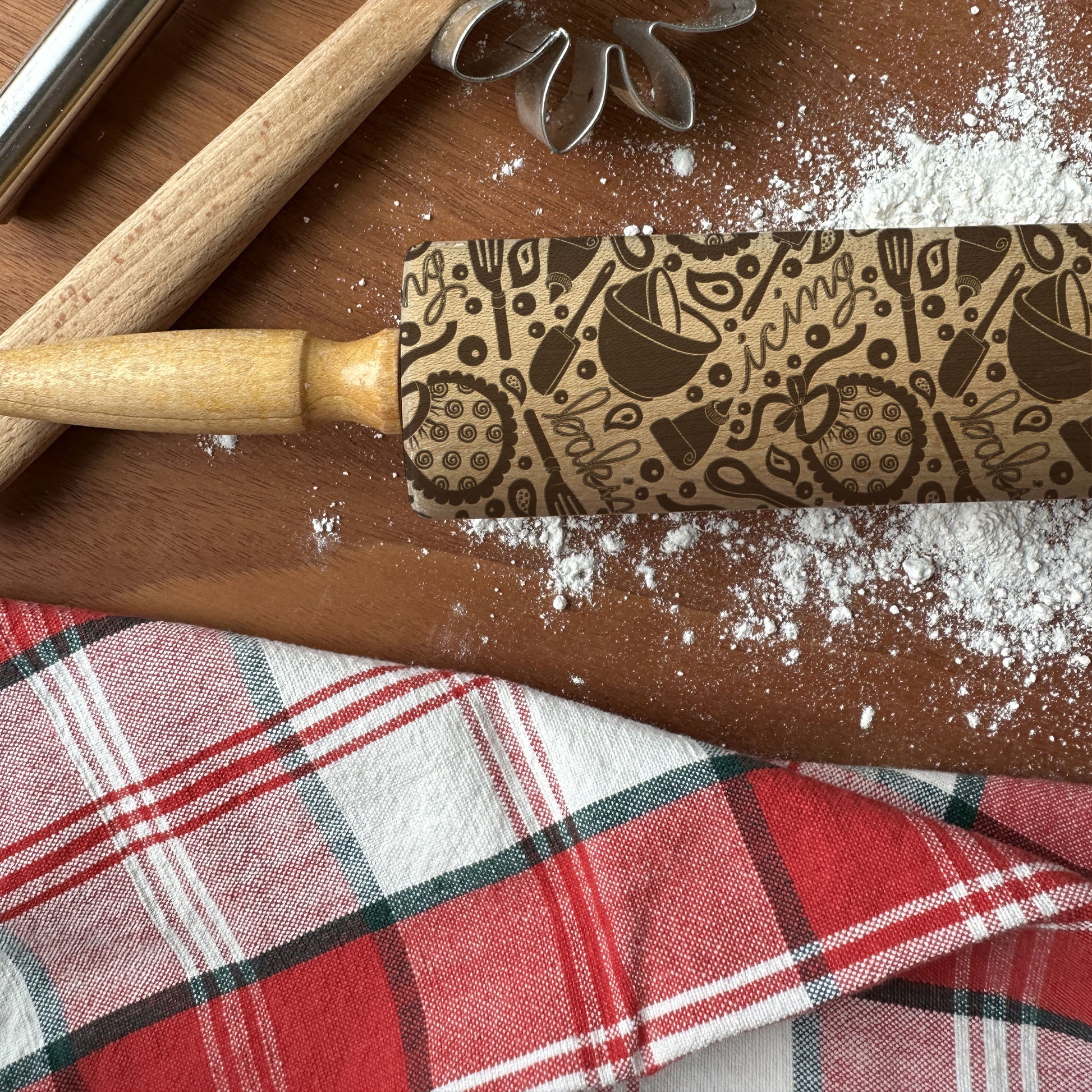 Patterned rolling pin on a wooden surface with flour and a plaid cloth.