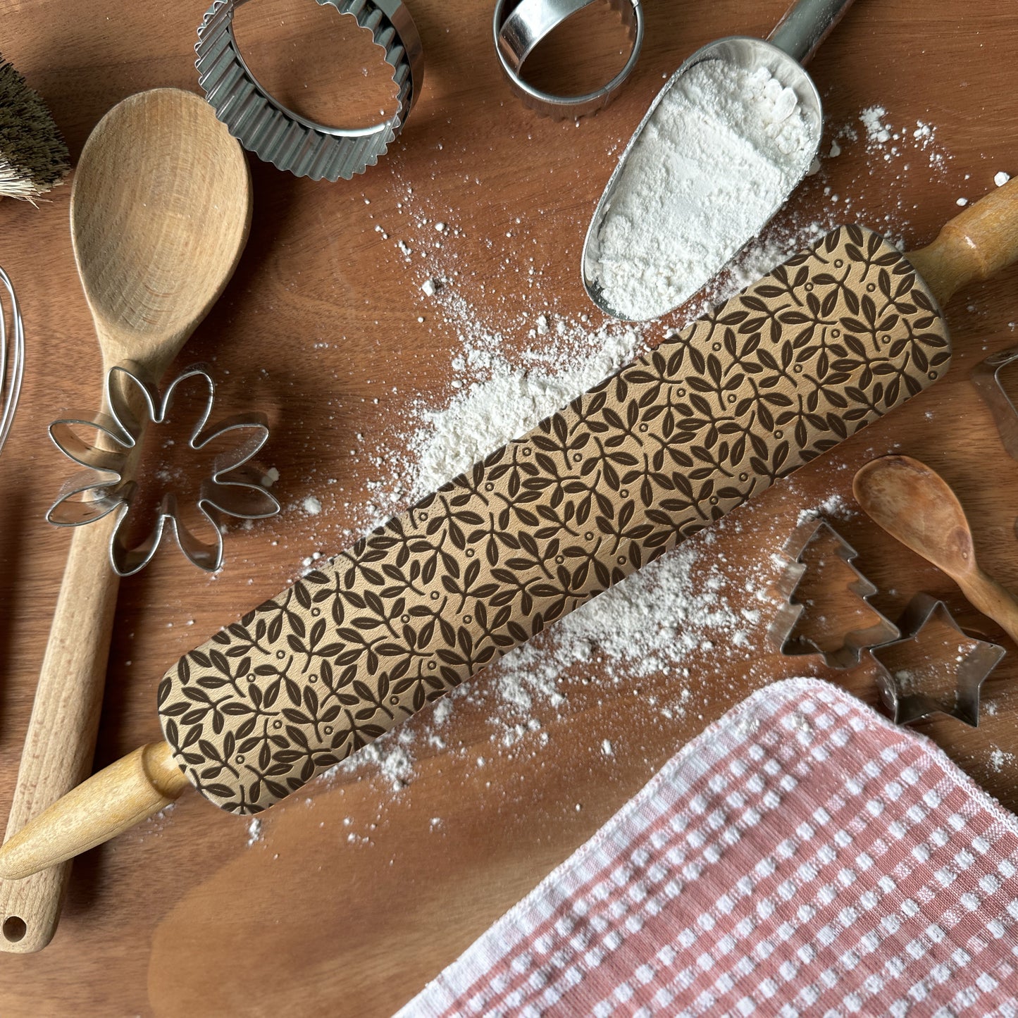 Wooden rolling pin with floral pattern on a wooden surface with flour and baking tools.