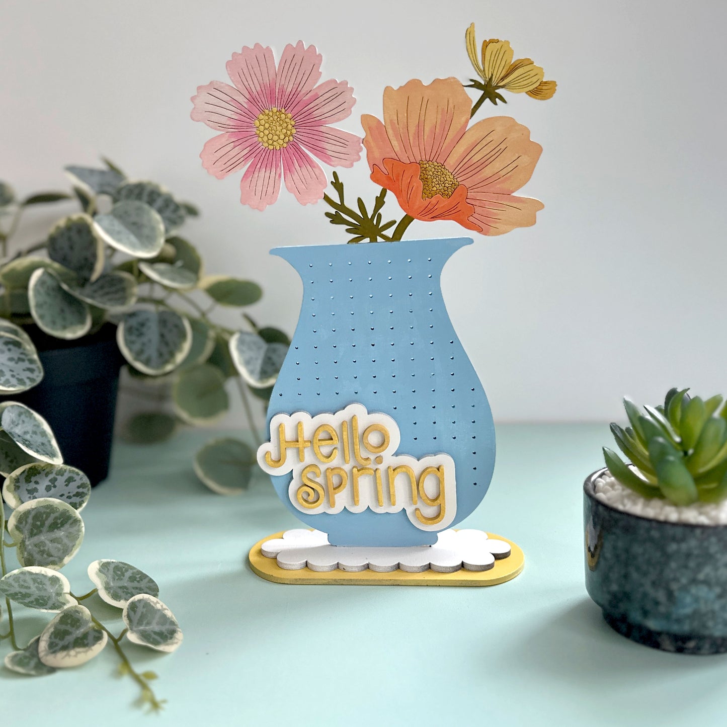 Decorative sign with 'Hello Spring' text and flowers on a light blue background