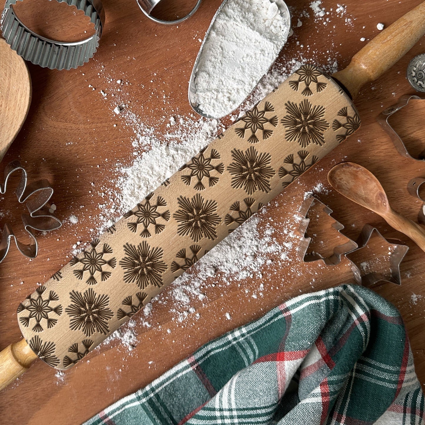 Baking tools including a rolling pin with star patterns, cookie cutters, and flour on a wooden surface.