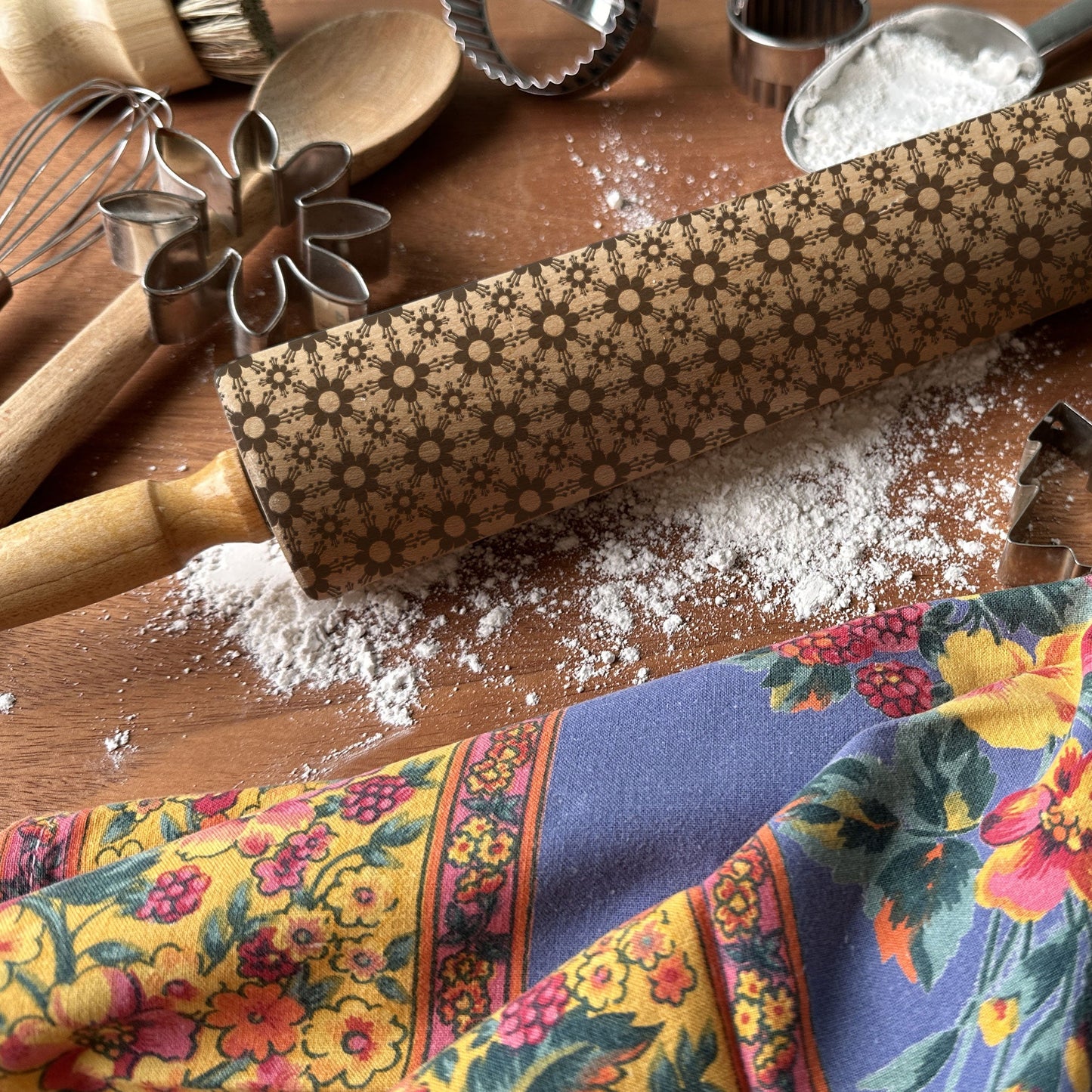 Baking tools including a rolling pin with a floral pattern on a wooden surface.