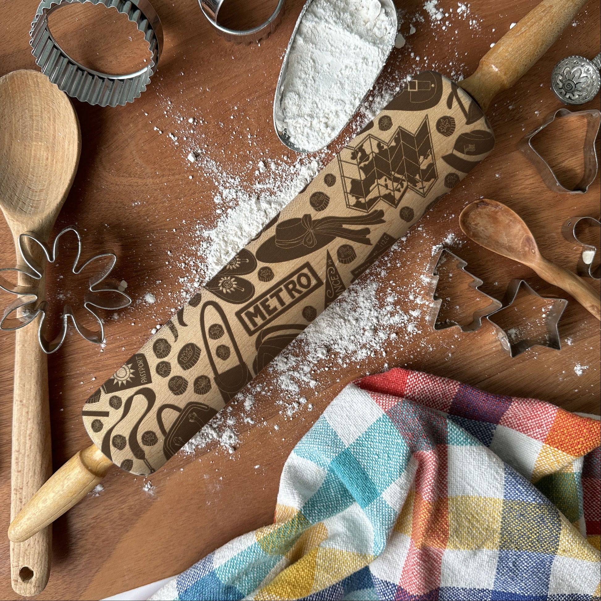 Baking tools including a rolling pin, wooden spoon, and cookie cutters on a wooden surface with flour.
